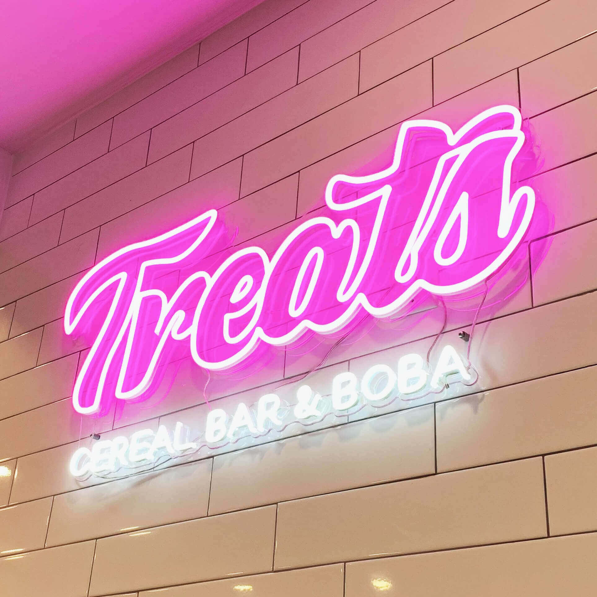 neon sign 桌布 壁紙 — 一個充滿活力的粉紅色霓虹燈招牌，上面寫著「Treats」，下方有白色字體，位於瓷磚牆上。