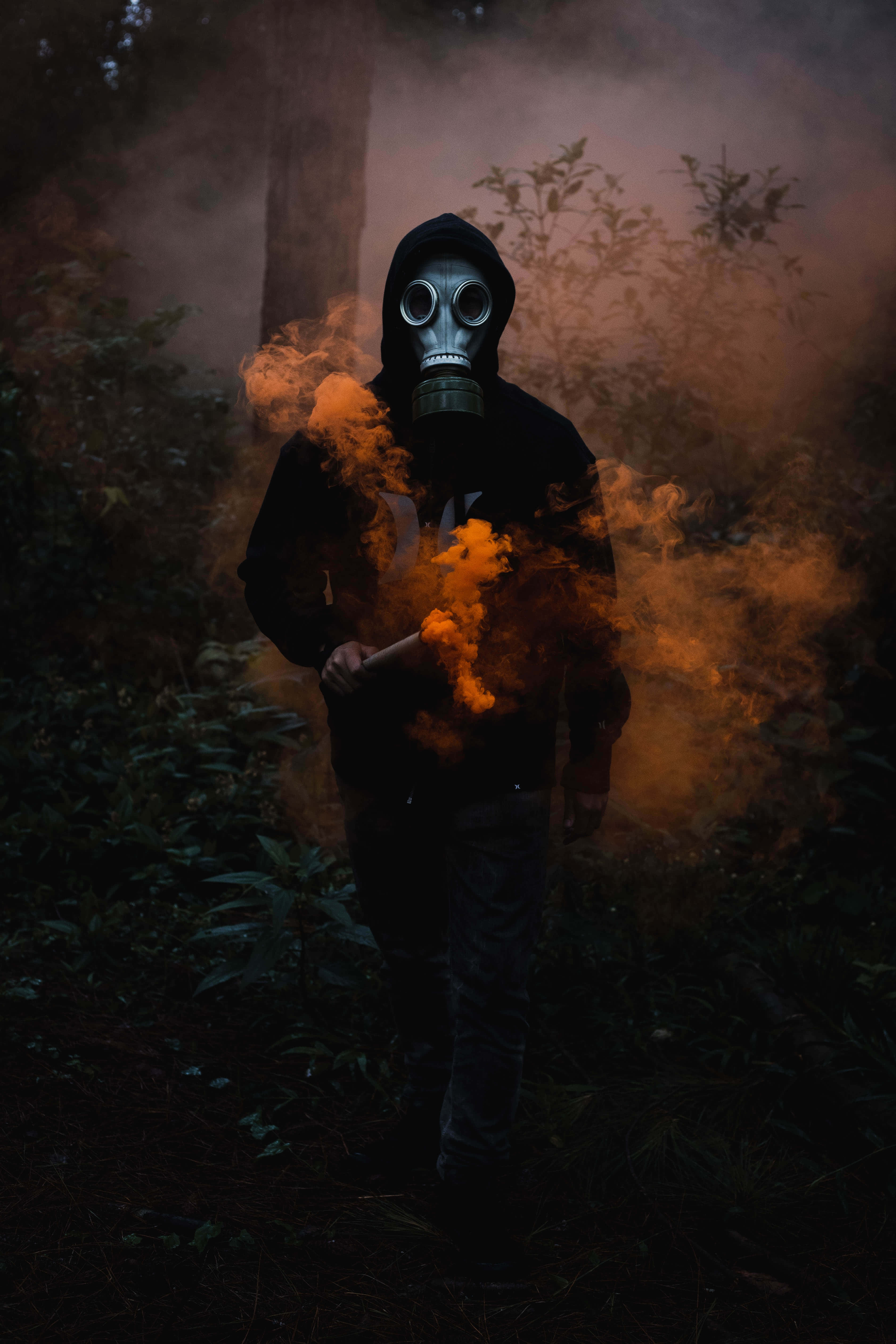 toxic 桌布 壁紙 — 一個戴著防毒面具和連帽衫的人物站在黑暗的森林中，被發光的橙色煙霧包圍。