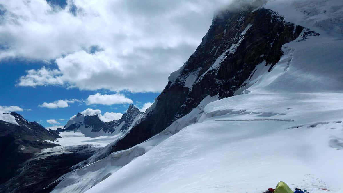 壁紙 — 一個孤獨的彩色帳篷坐落在積雪的山坡上，天空部分多雲，呈現藍色。