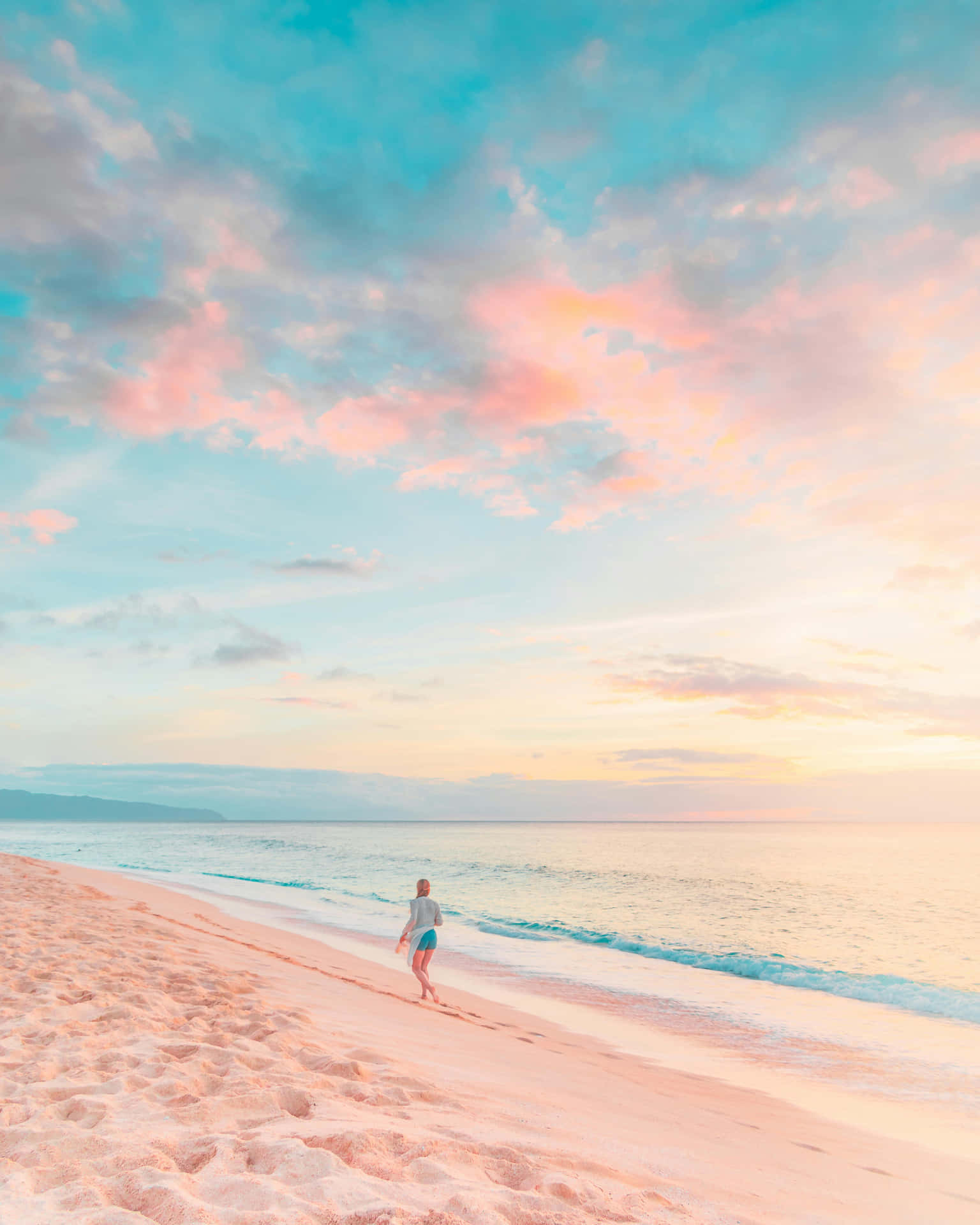 Preppy Beach 桌布 壁紙 — 一個孤獨的人沿著粉紅色沙灘漫步，夕陽西下，柔和色彩的雲彩倒映在平靜的海面上。