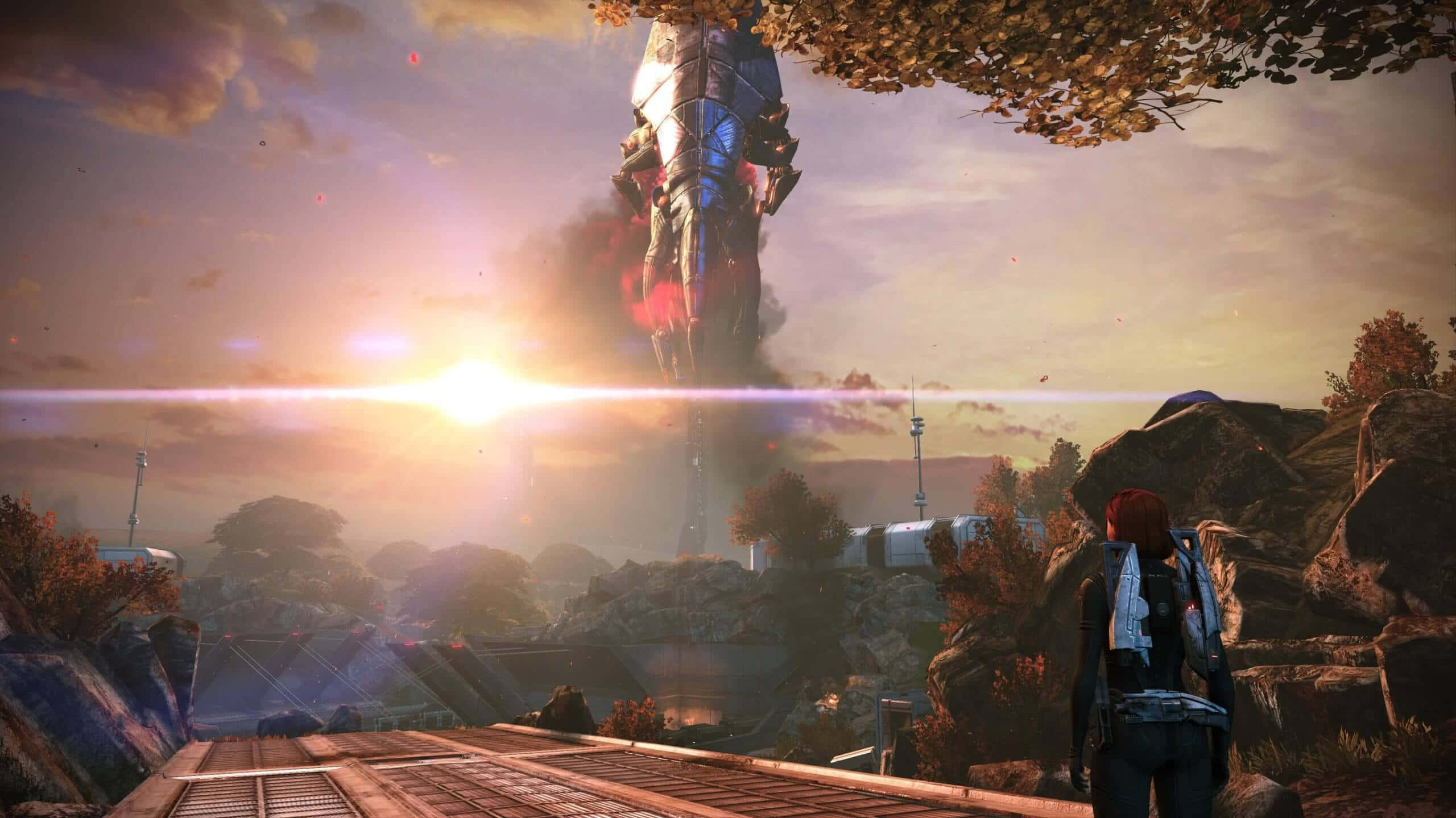 Mass Effect Legendary Edition 桌布 壁紙 — 一個孤獨的身影站在木製平台上，凝視著一座從岩石景觀中升起、高聳的未來風格機甲，背景是日落。