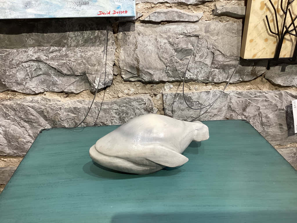  壁紙 — 一個光滑的白色鯨魚雕塑放在一張青綠色桌子上，背景是粗糙的灰色石牆。