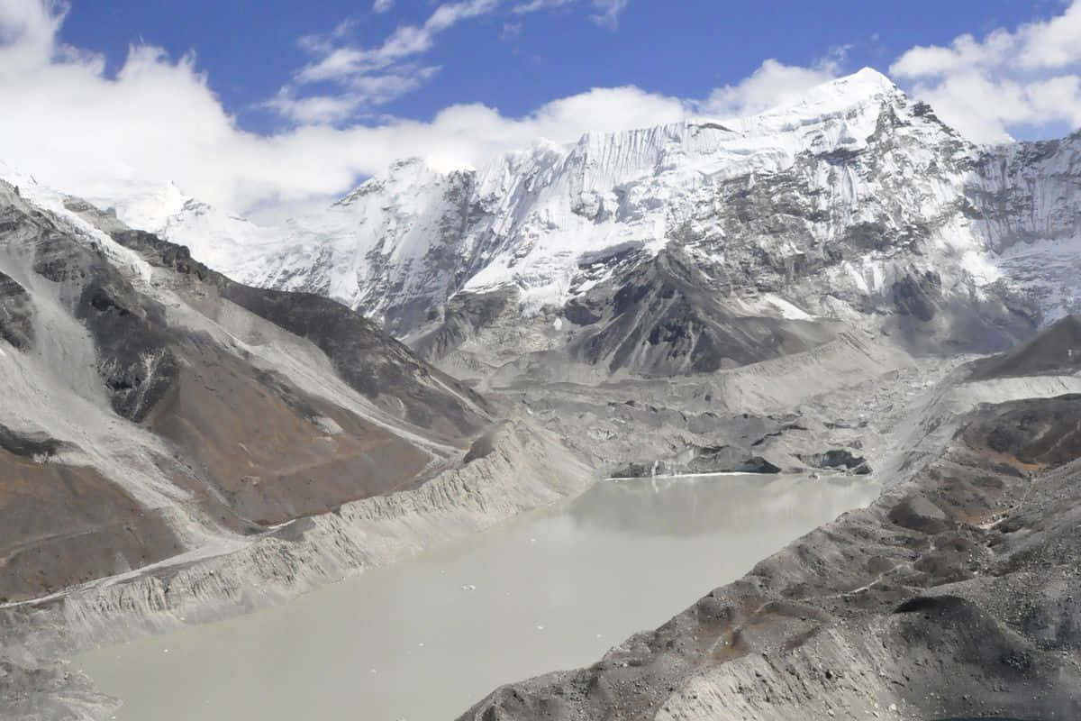  壁紙 — 一個廣闊的冰川湖，坐落在崎嶇的雪山之中，天空湛藍，白雲朵朵。