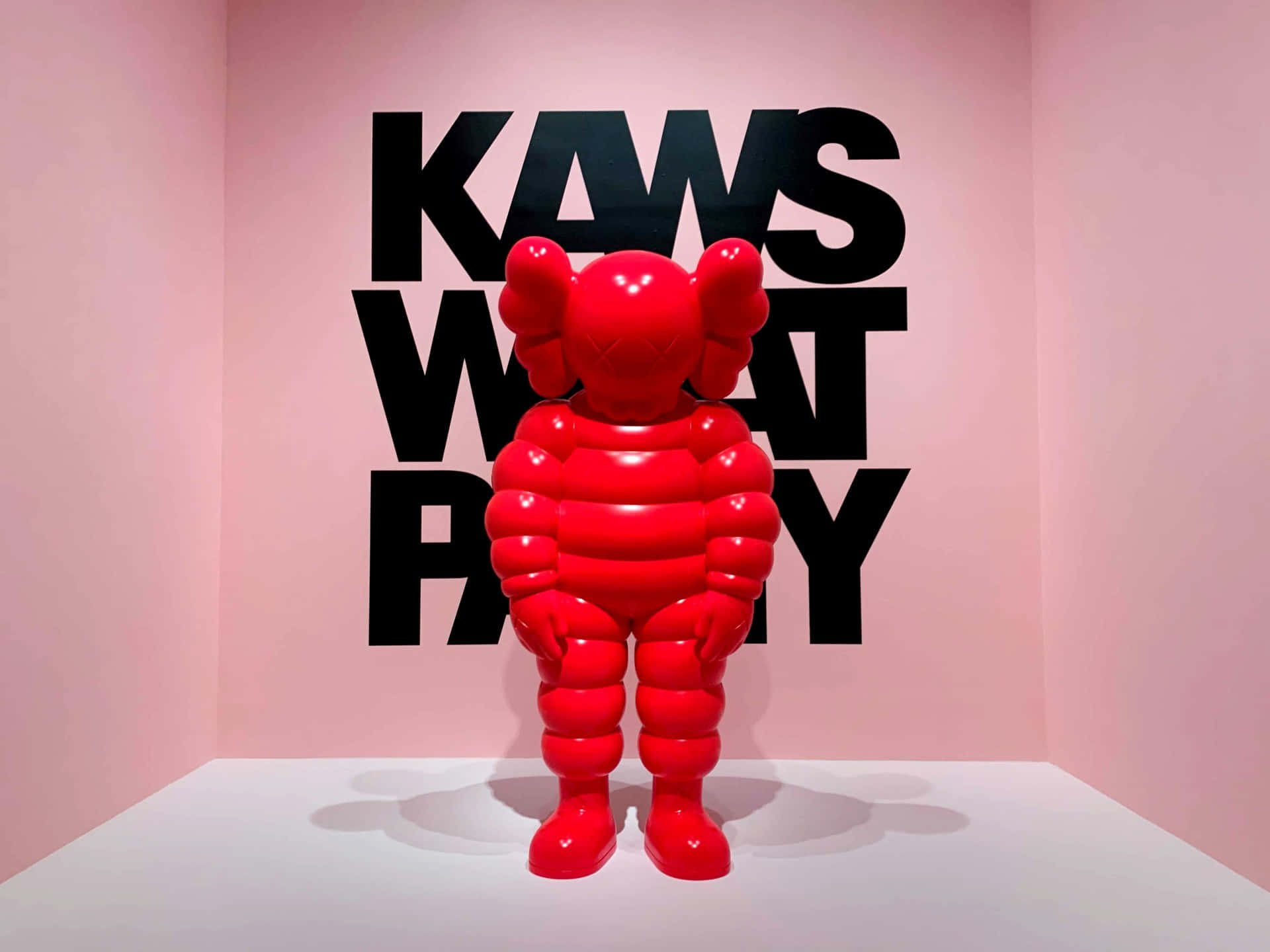 畫廊中的紅色KAWS雕塑，粉紅色牆壁和黑色文字。 — Kaws 壁紙