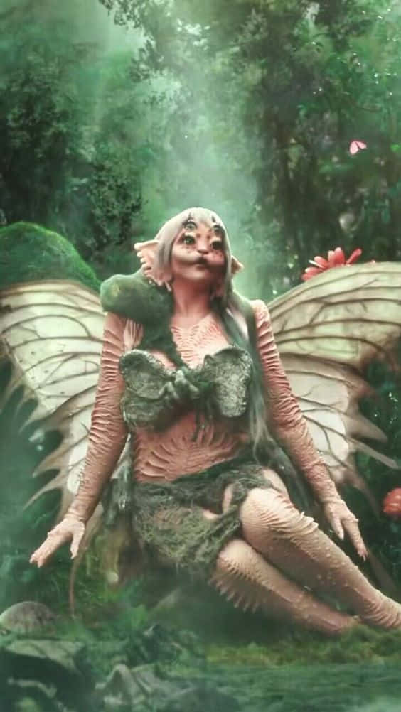  壁紙 — 一個幻想中的仙女，擁有像飛蛾般的大翅膀，安詳地坐在霧氣瀰漫的綠色森林中，周圍環繞著苔蘚和發光的植物。