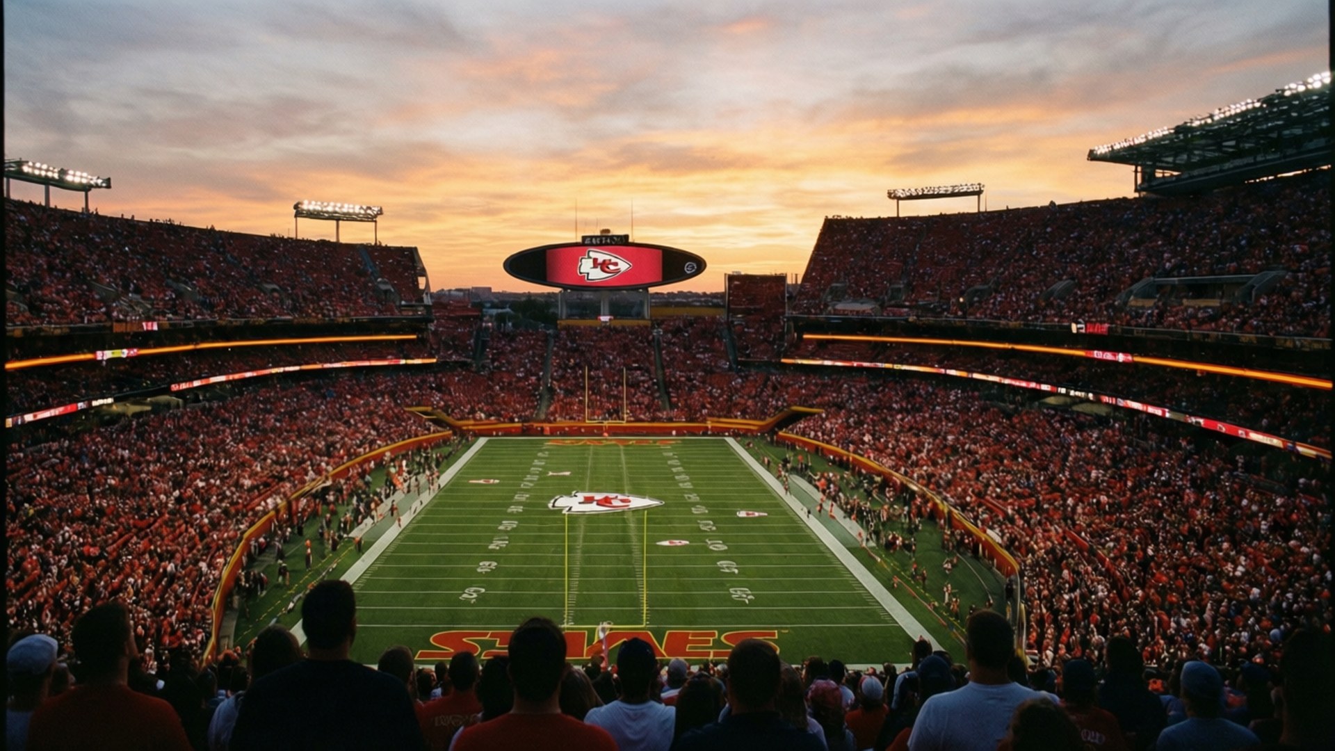 Stadium Sunset 壁紙 — 一個擠滿球迷的足球場，日落時分，紅色球迷擠滿看台，圍繞著帶有球隊標誌的綠色球場。