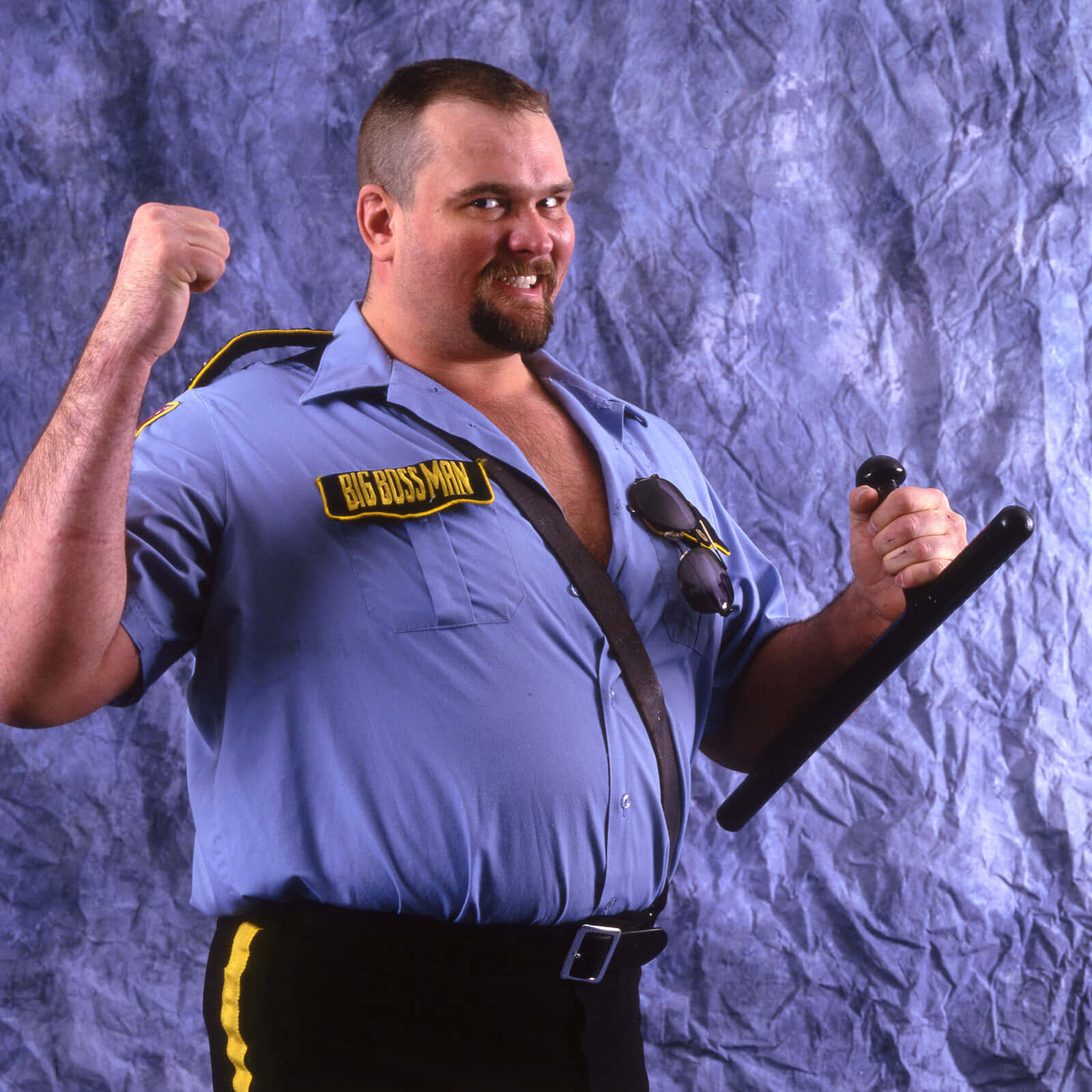 壁紙 — 一個肌肉發達的男人穿著藍色「Big Boss Man」襯衫，在皺巴巴的紫色背景下彎曲手臂，手持警棍。