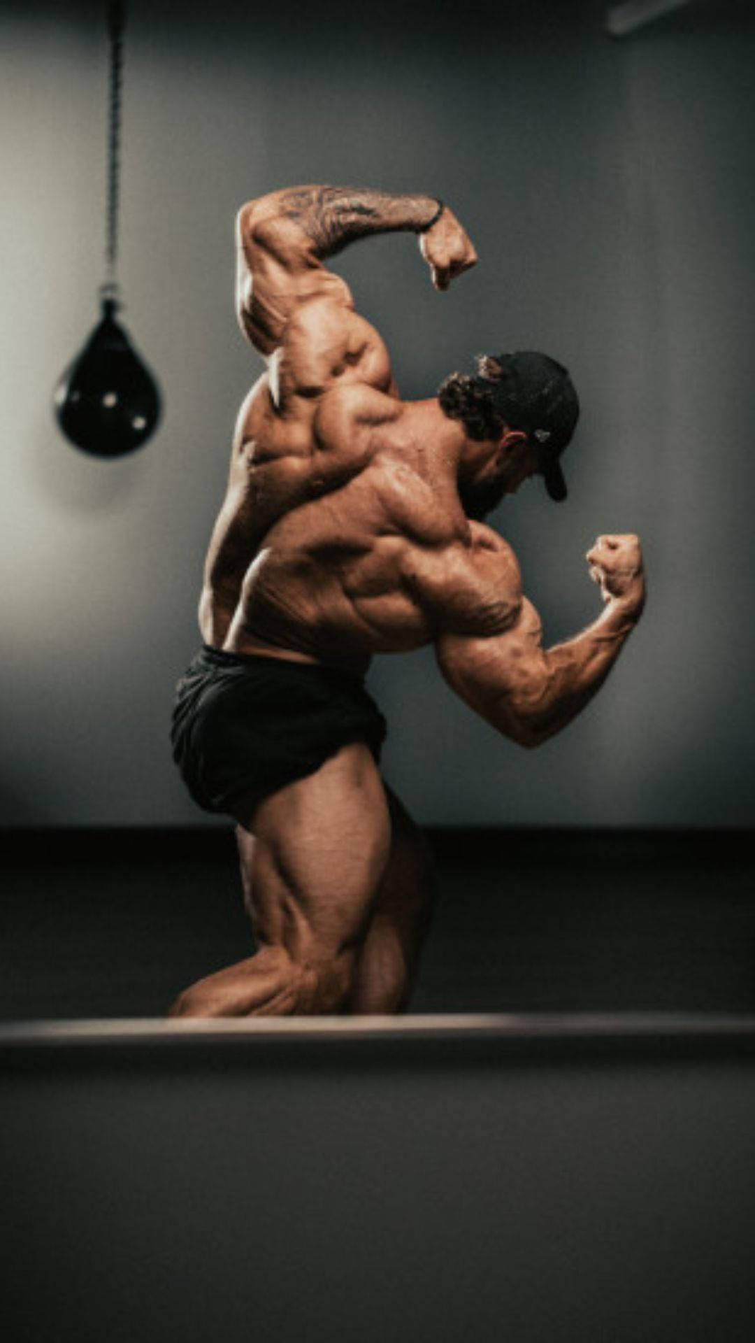 一個肌肉發達的男人在健身房繃緊背部和手臂。 — Chris Bumstead 壁紙