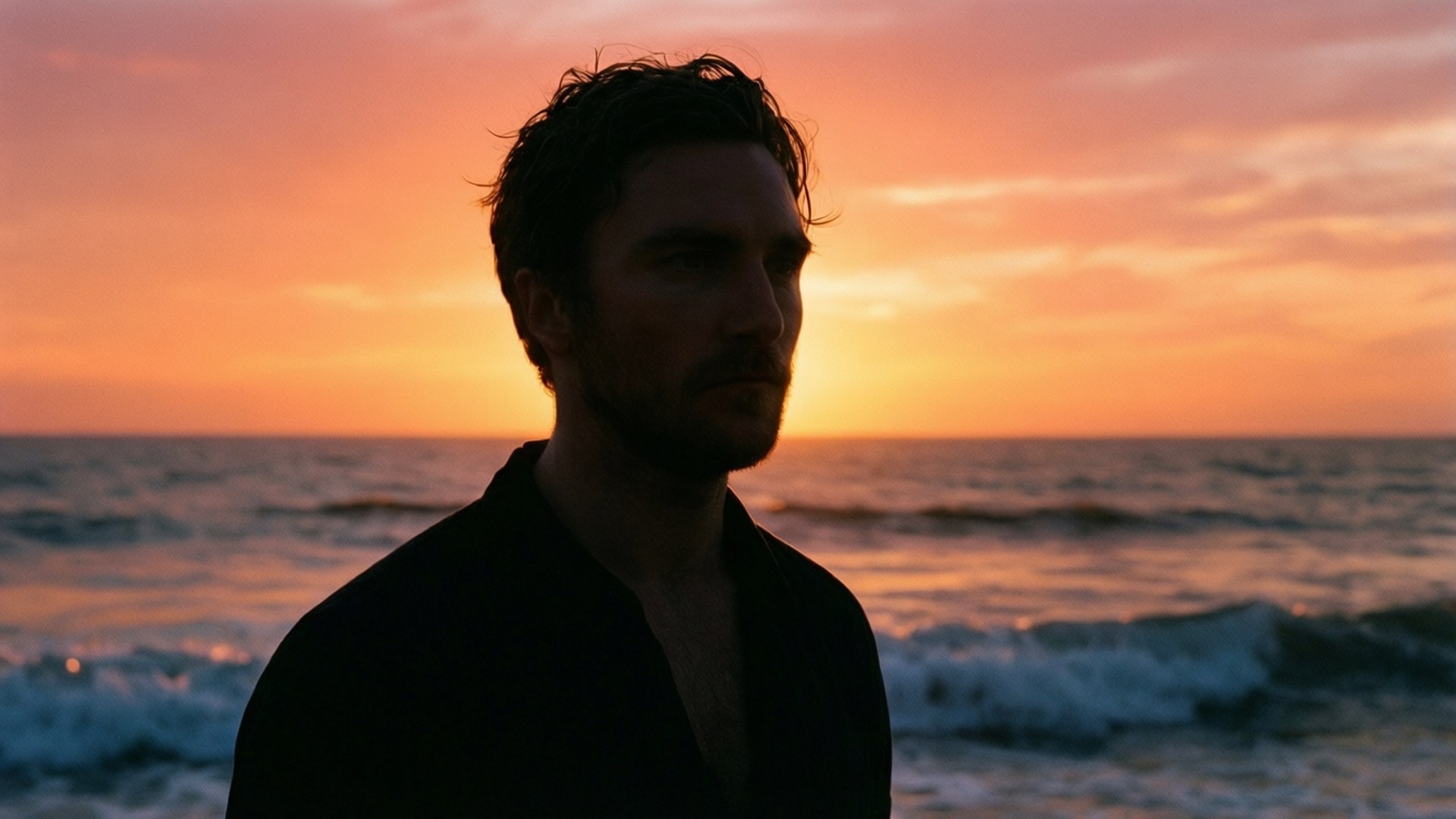 Beach Sunset Silhouette 壁紙 — 一個男人以剪影姿態站立，背景是海洋上 vibrant 的橙色和粉紅色日落，伴隨著溫柔的波浪。