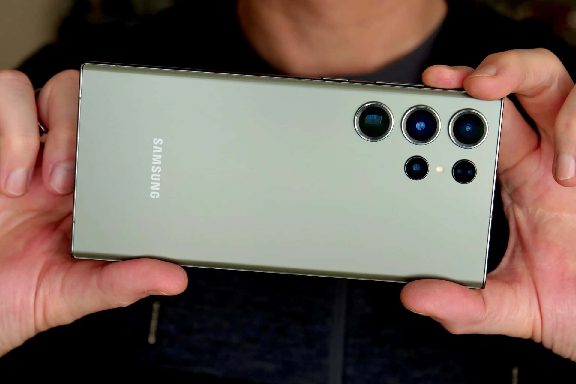  壁紙 — 一個人手持一款時尚的銀色Samsung智慧型手機，展示其多鏡頭相機陣列和極簡設計。