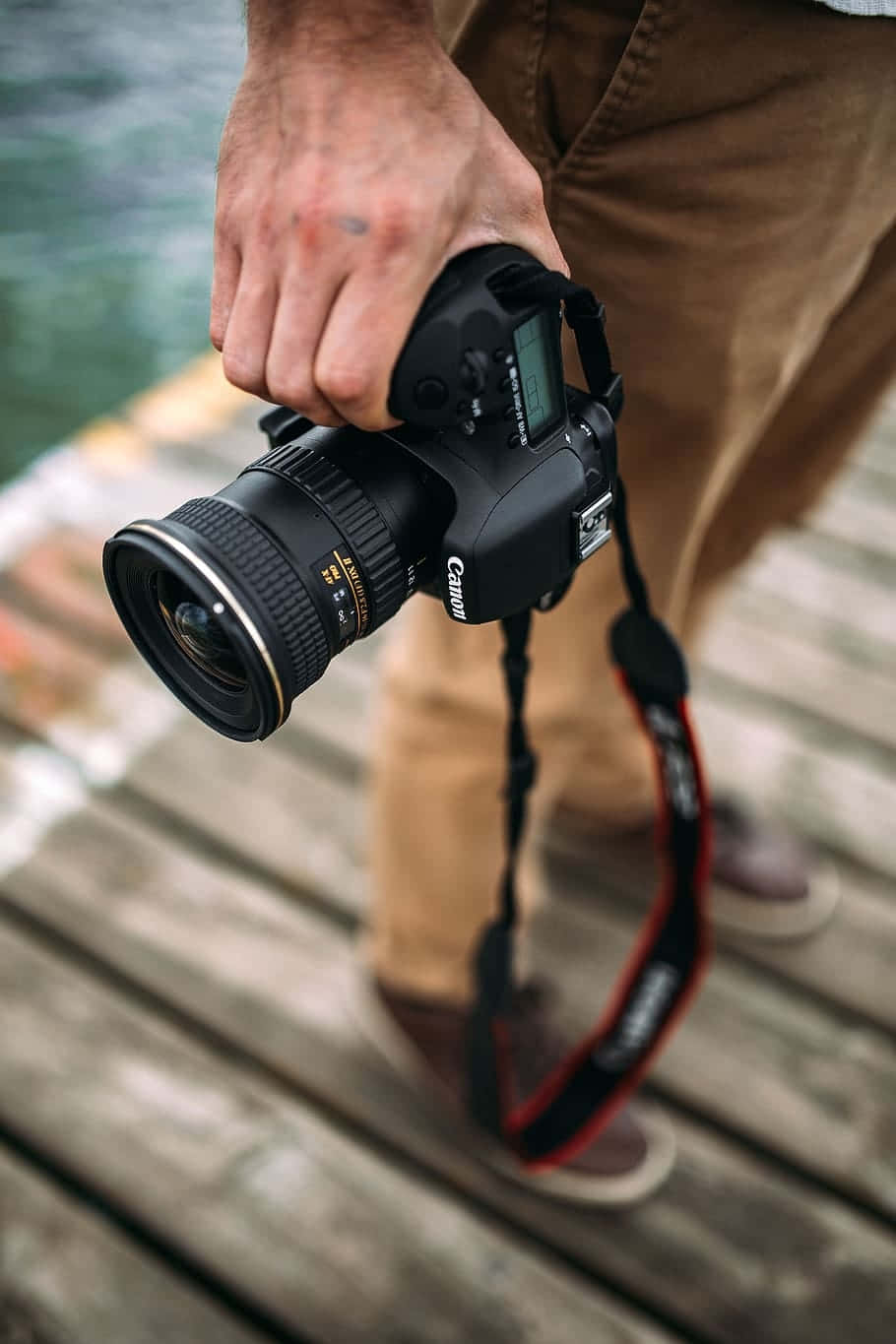 Cameraman 桌布 壁紙 — 一個人在水邊的木碼頭上，手持一部黑色Canon DSLR相機，配有大鏡頭。
