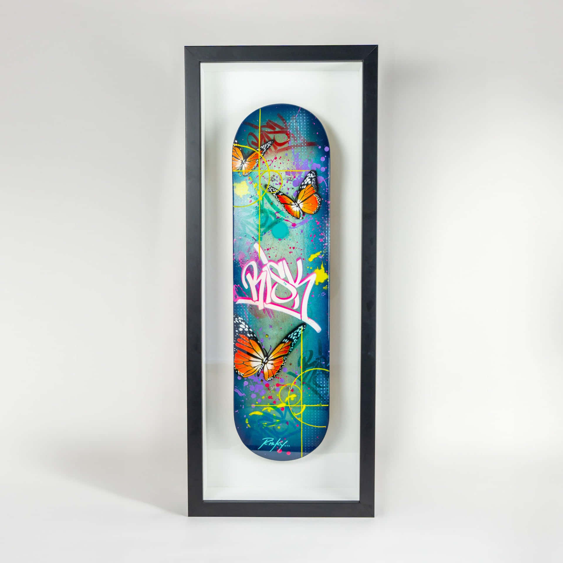  壁紙 — 一個色彩鮮豔的滑板甲板，上面有橙色蝴蝶和塗鴉藝術，展示在白色牆壁上的黑色框架中。