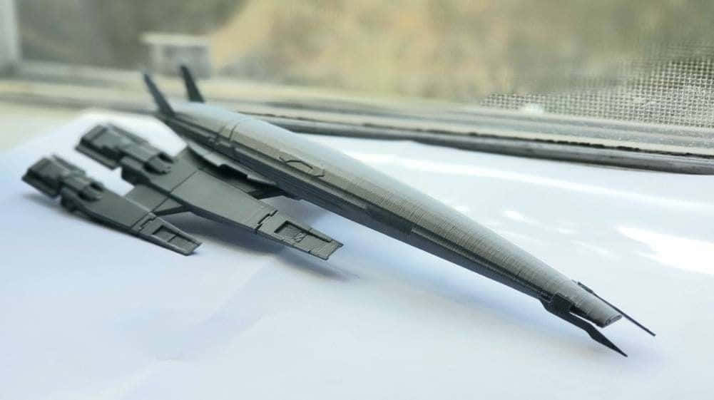 Normandy Sr-2 桌布 壁紙 — 一個時尚的黑色3D列印未來太空船模型放在白色表面上，靠近一個有模糊室外景觀的窗戶。