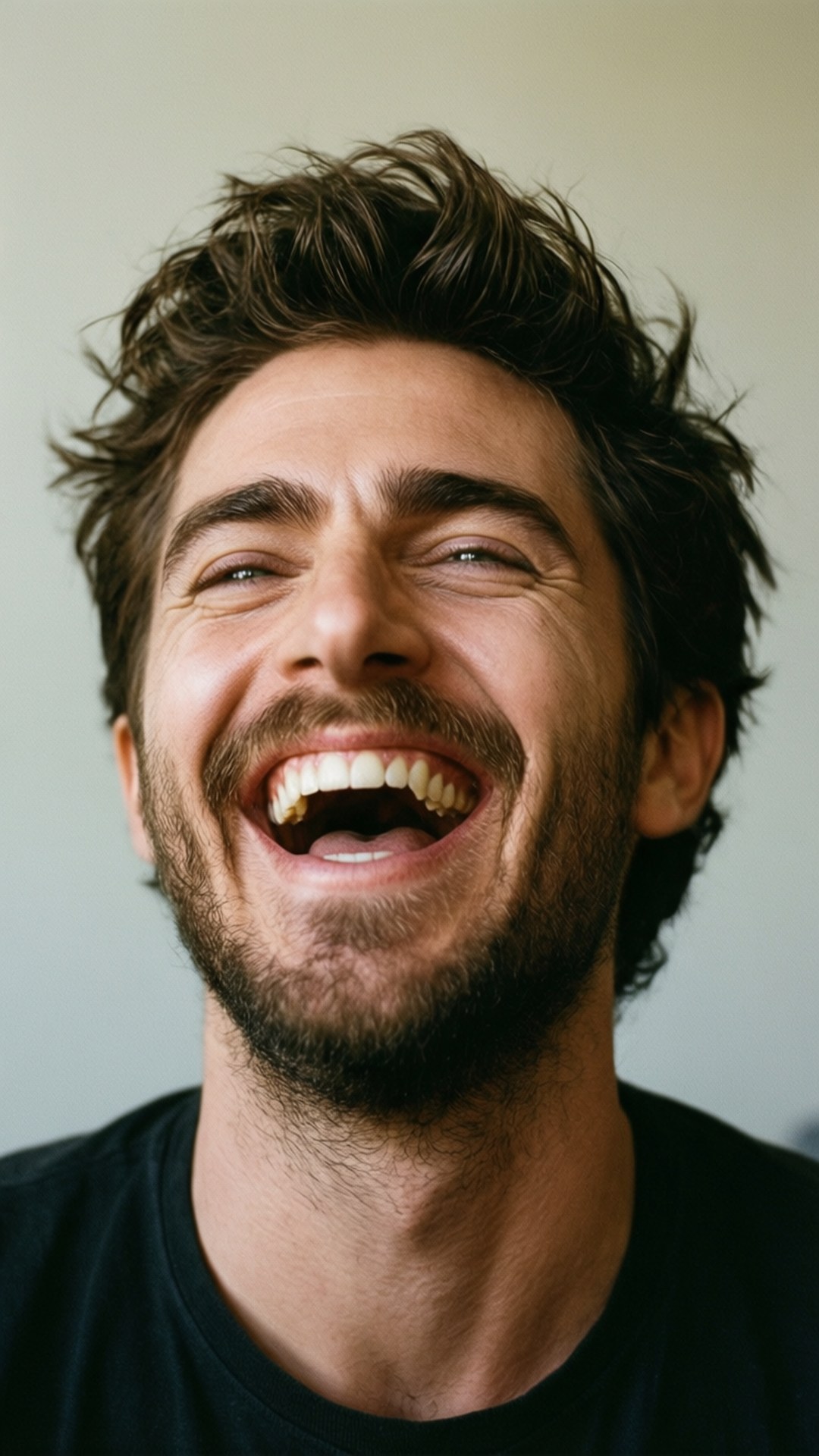 Hearty Laugh Portrait 壁紙 — 一個頭髮凌亂、留著鬍子的男人在淺灰色背景前開懷大笑。