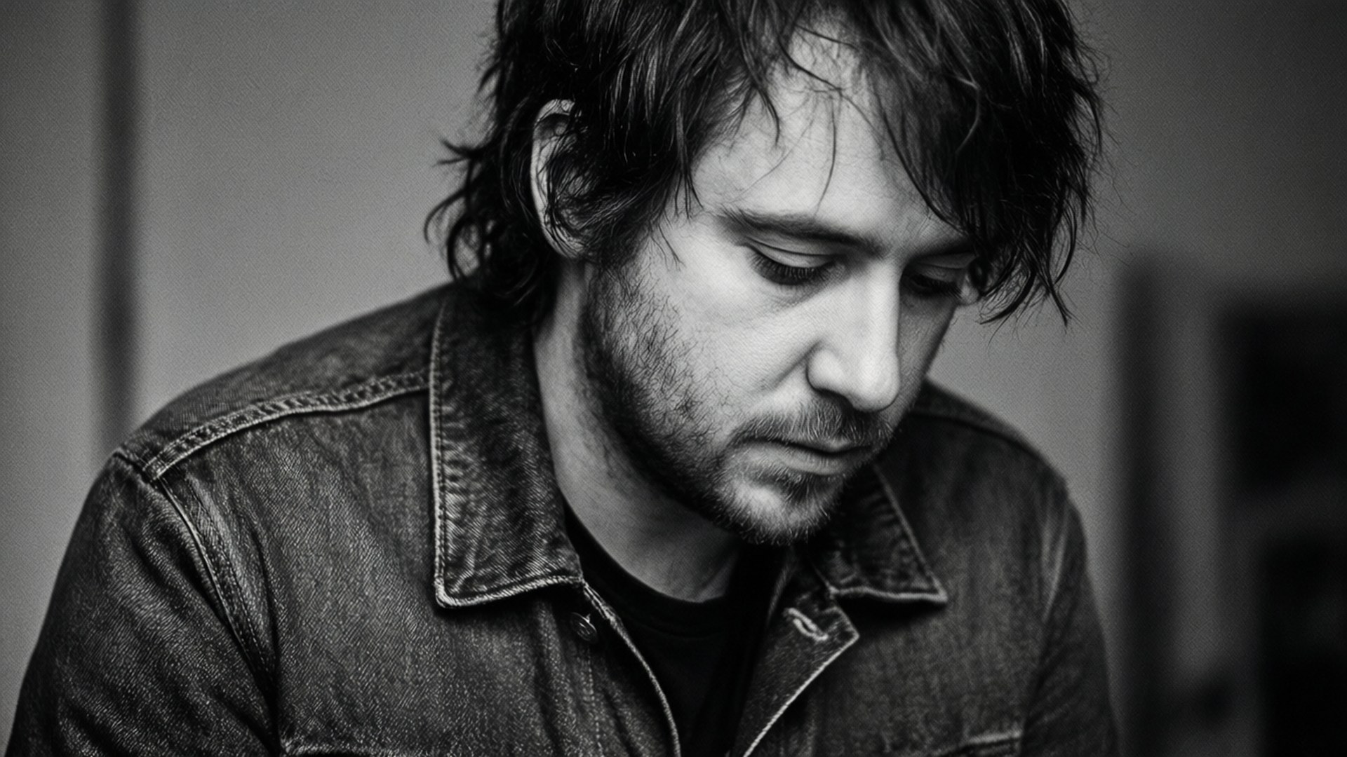 Contemplative Grayscale 壁紙 — 一個頭髮蓬鬆、身穿牛仔外套的男人低頭沉思的黑白肖像。