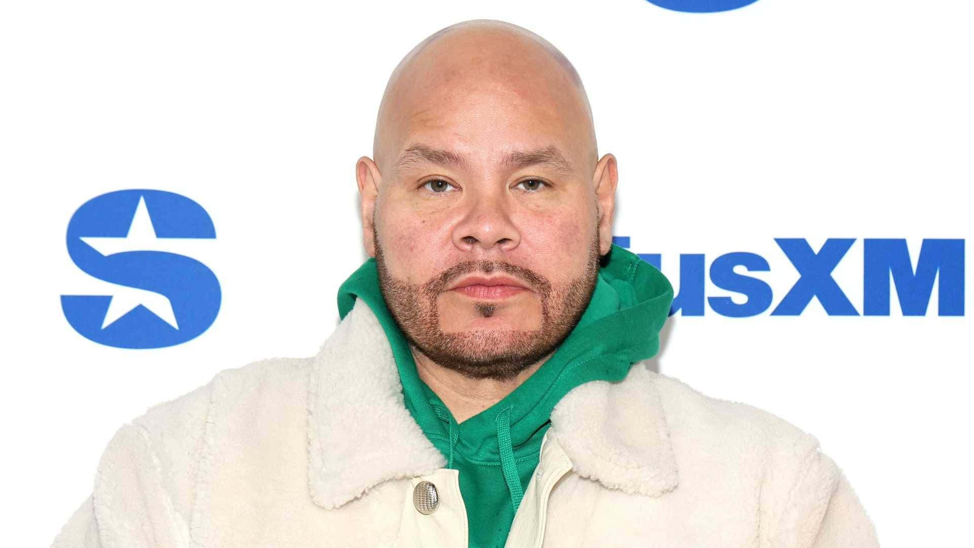 壁紙 — 一個禿頭留山羊鬍的男人，在白色背景上穿著奶油色羊羔絨外套，內搭綠色連帽衫，背景有藍色SiriusXM標誌。