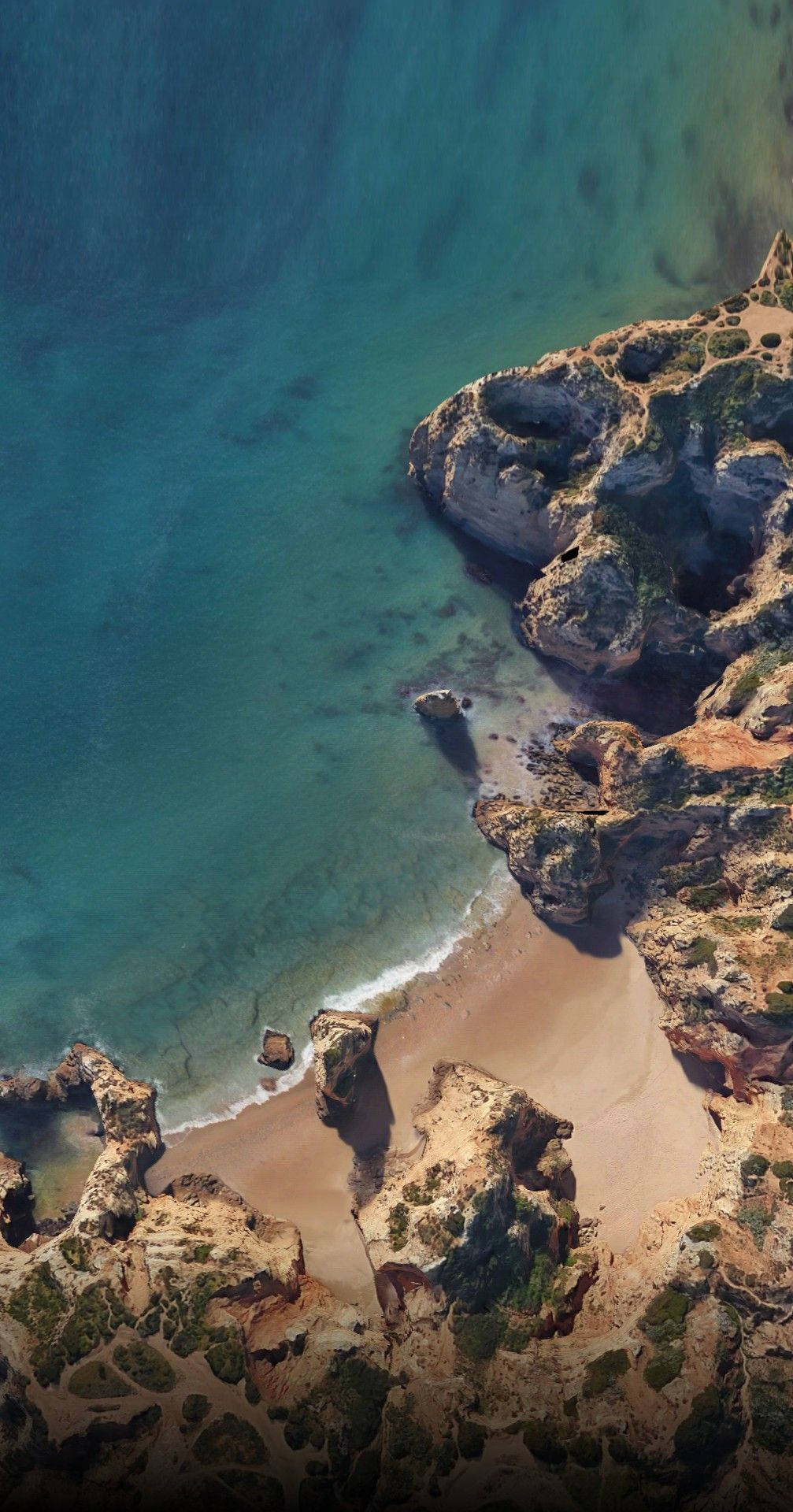 一個隱蔽海灘的鳥瞰圖，有碧綠色的海水和岩石懸崖。 — Google pixel 壁紙