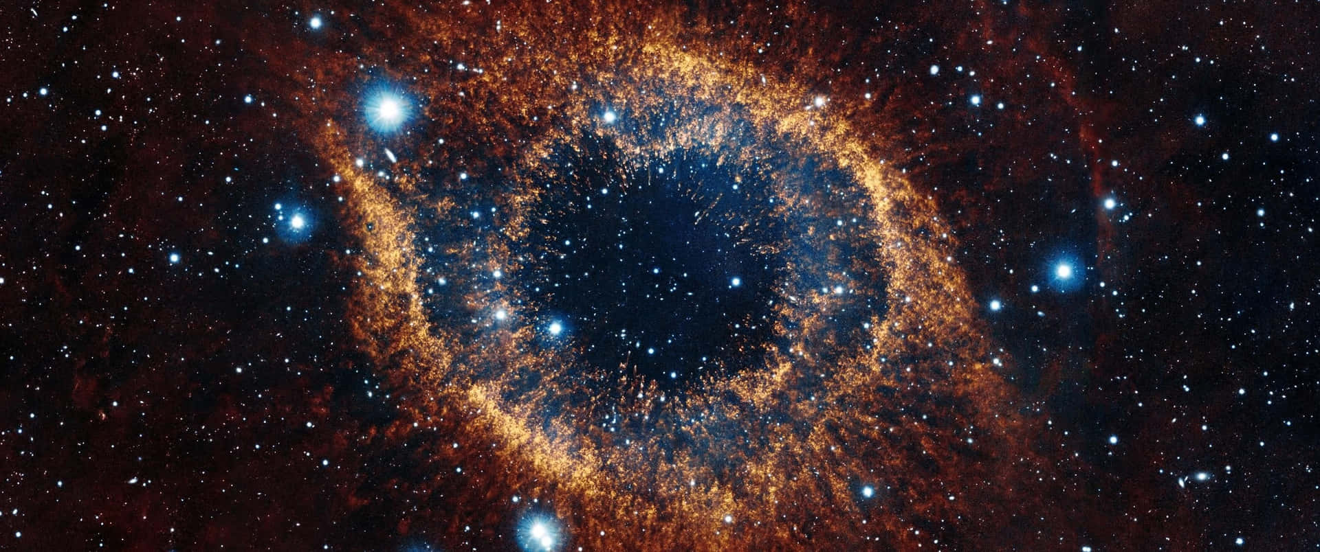 在深空中，眼形星雲在星群中散發出橙色和藍色的光芒。 — 3440X1440 壁紙