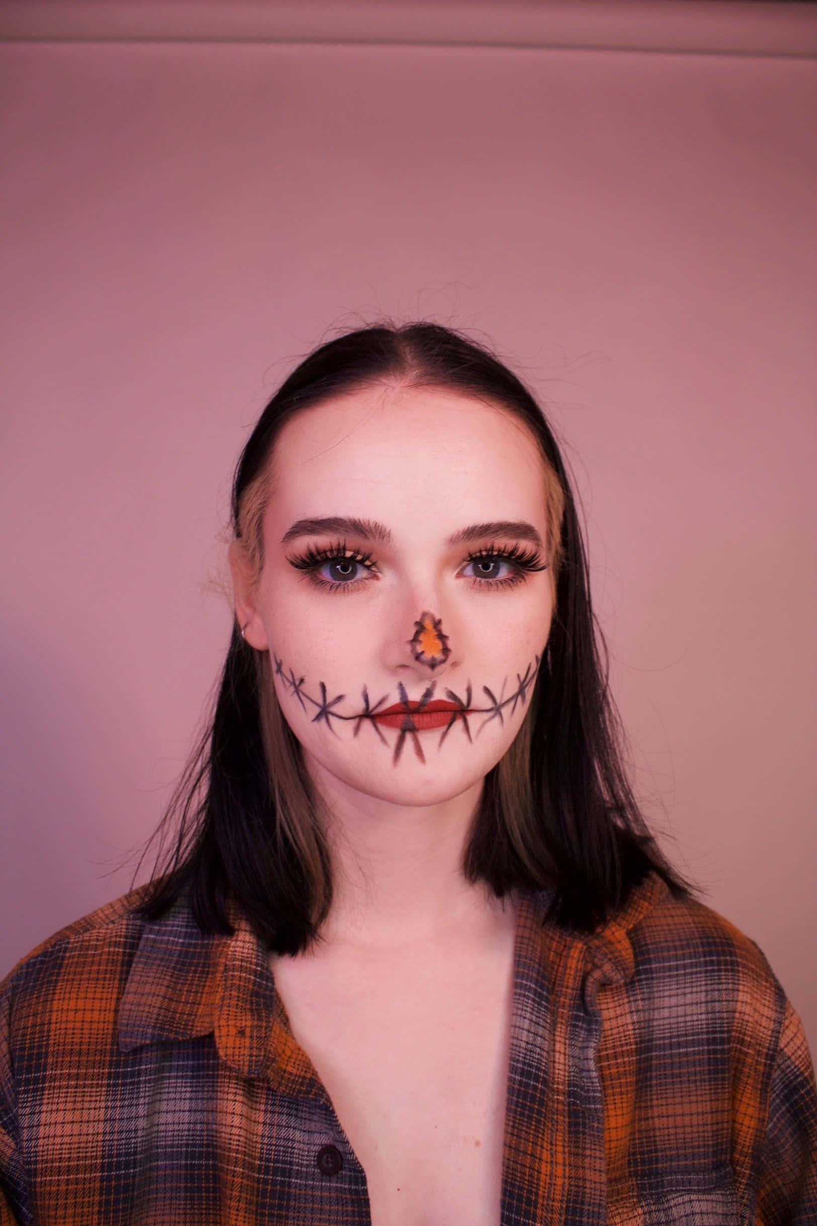 Halloween Face Paint 桌布 壁紙 — 一個嘴巴和鼻子縫合妝容的人，穿著格子襯衫，在柔和的粉紅色背景前擺姿勢。