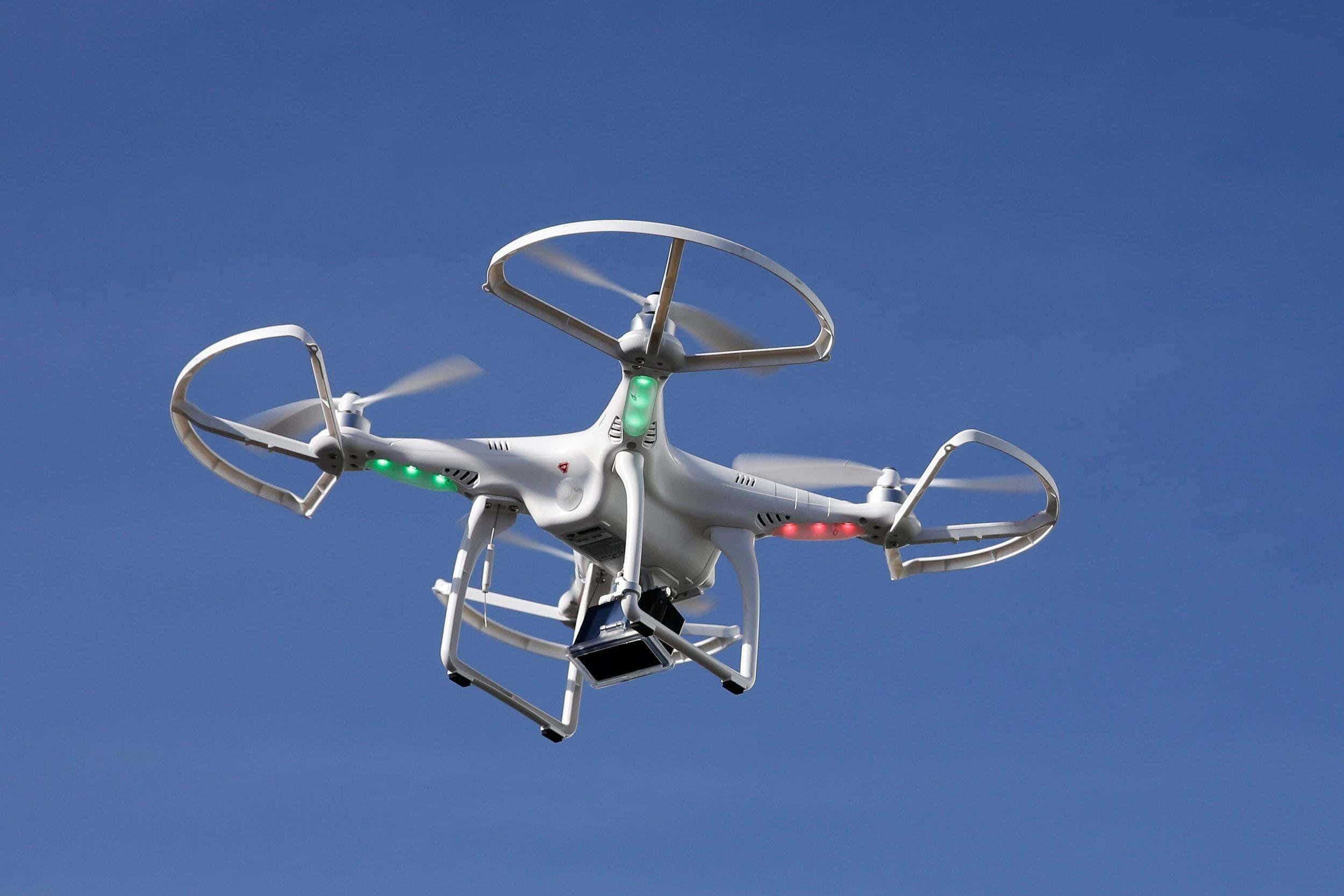 Drone Camera 桌布 壁紙 — 一架白色四軸無人機，帶有保護框架和發光燈光，在晴朗的藍天中盤旋。