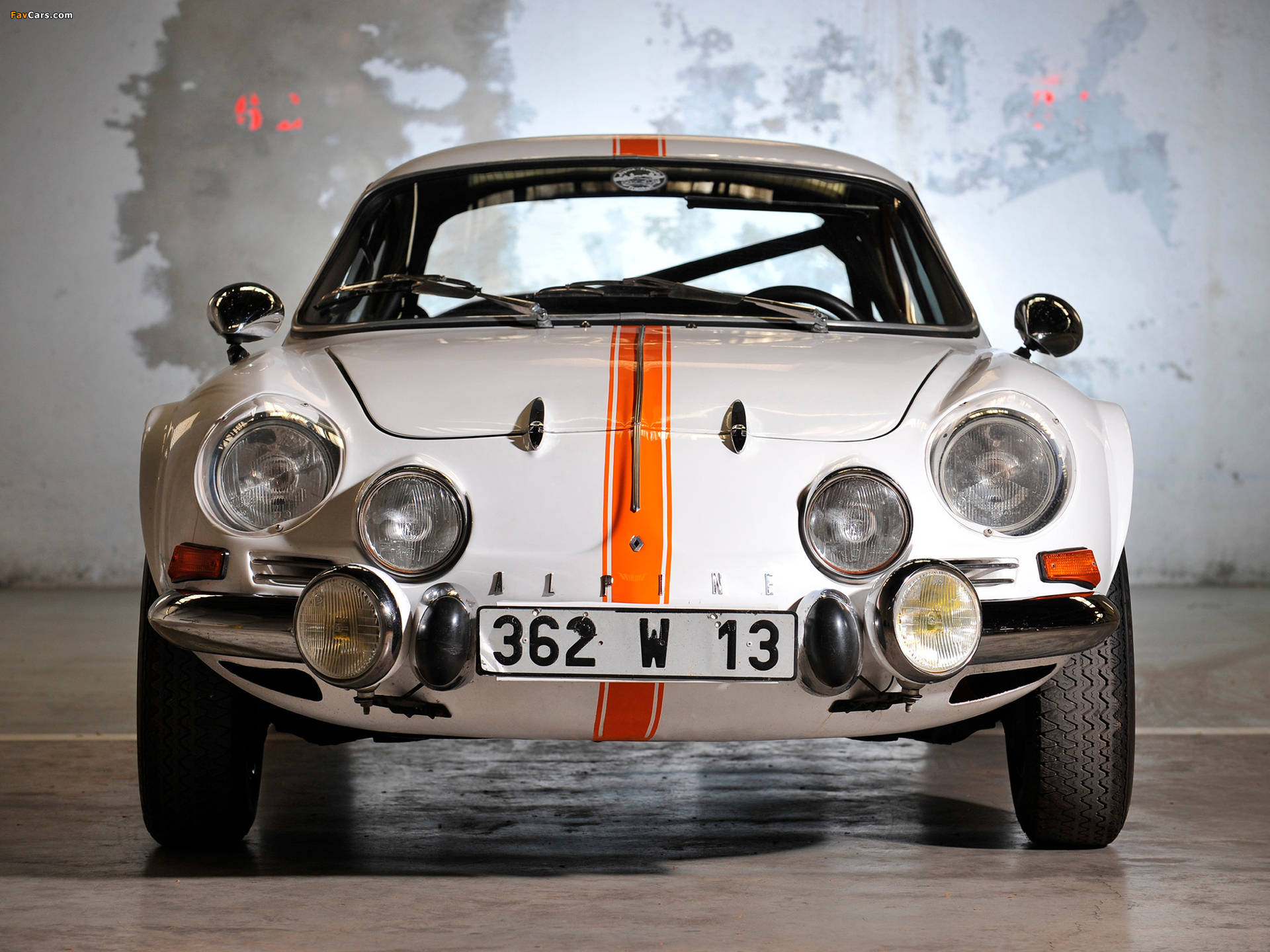 在混凝土車庫中，帶有橙色條紋的復古白色Alpine A110賽車。 — F1 壁紙