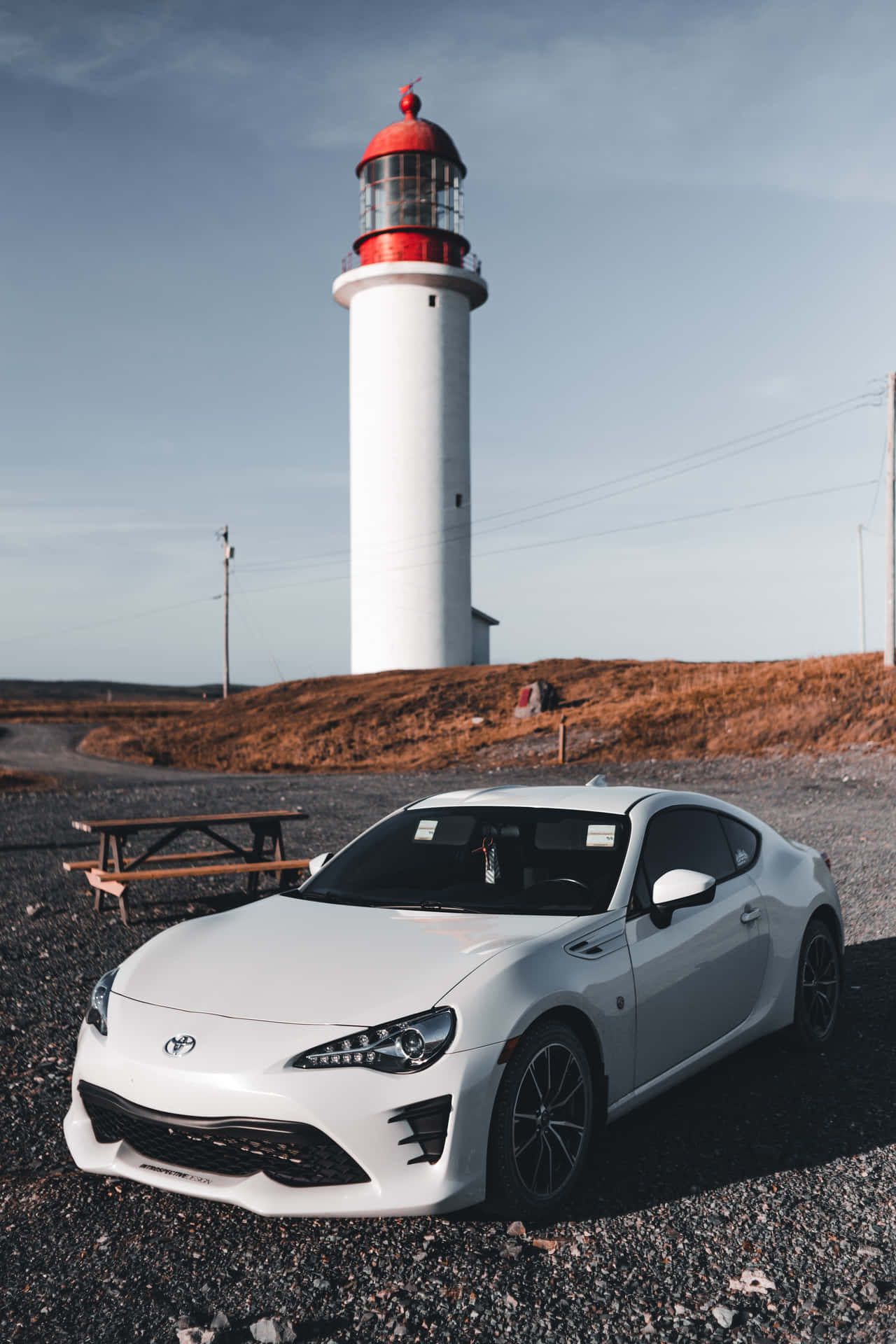 陽光明媚的日子裡，白色跑車停泊在海岸燈塔附近。 — Toyota Supra 壁紙