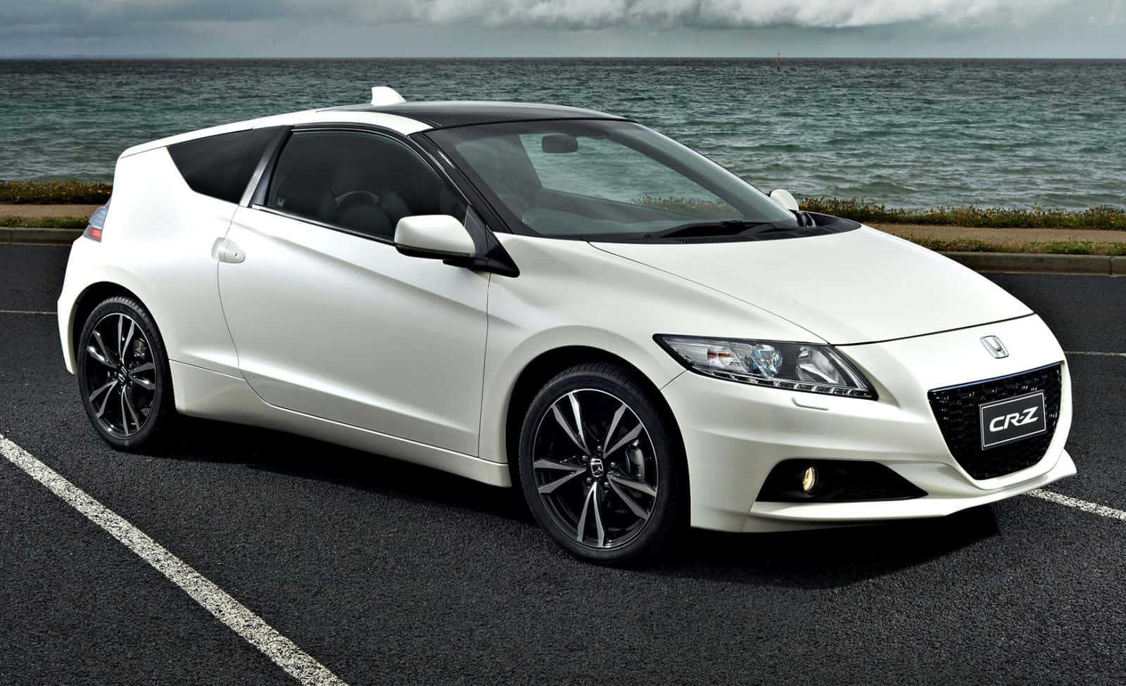 Honda Cr-z 桌布 壁紙 — 一架流線型的白色本田CRZ跑車停在瀝青停車場上，背景有海浪和陰天。