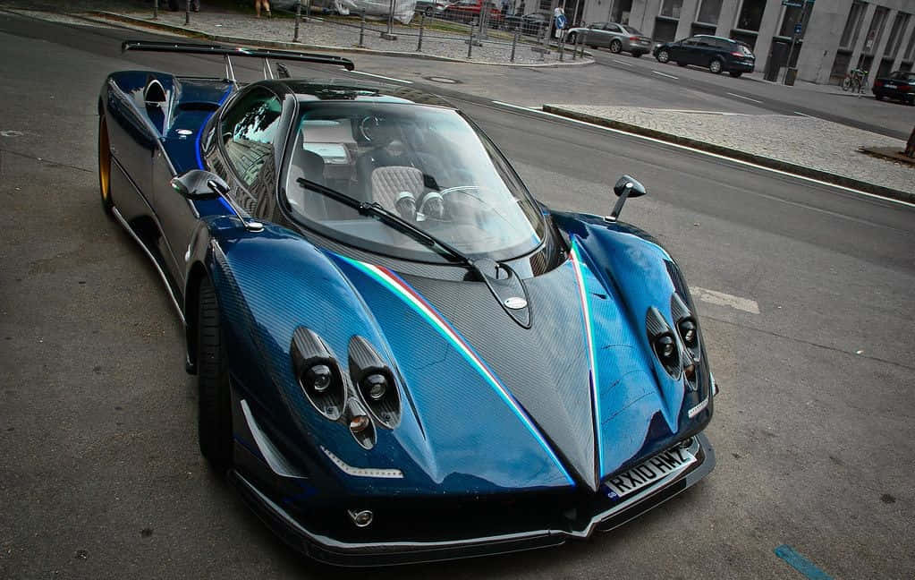 Pagani Zonda Tricolore 桌布 壁紙 — 一架流線型藍色碳纖維跑車，帶有彩虹條紋，停泊在城市街道上。