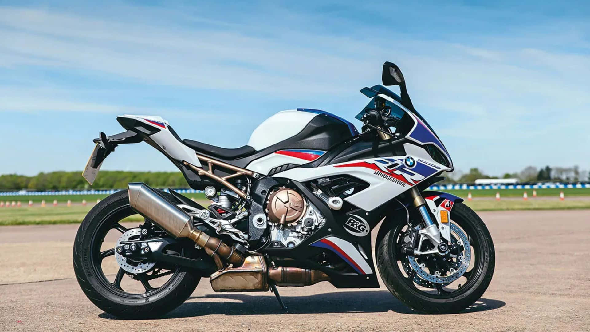  壁紙 — 一架時尚的白、藍、紅 BMW S1000RR 重機停放在賽車場上，天空清澈湛藍。