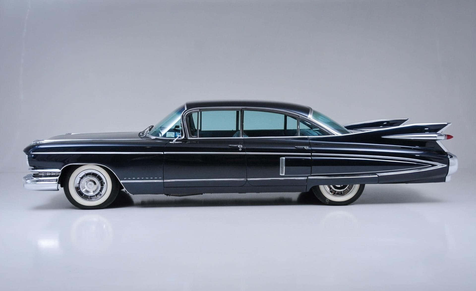 Cadillac Fleetwood 桌布 壁紙 — 一架時尚的黑色1950年代凱迪拉克，配備鍍鉻飾邊和白牆輪胎，矗立在簡約的工作室環境中。