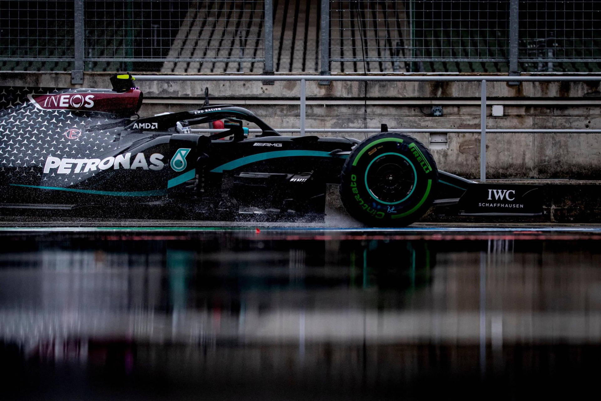 黑色和藍綠色一級方程式賽車在潮濕賽道上飛馳濺水。 — F1 壁紙