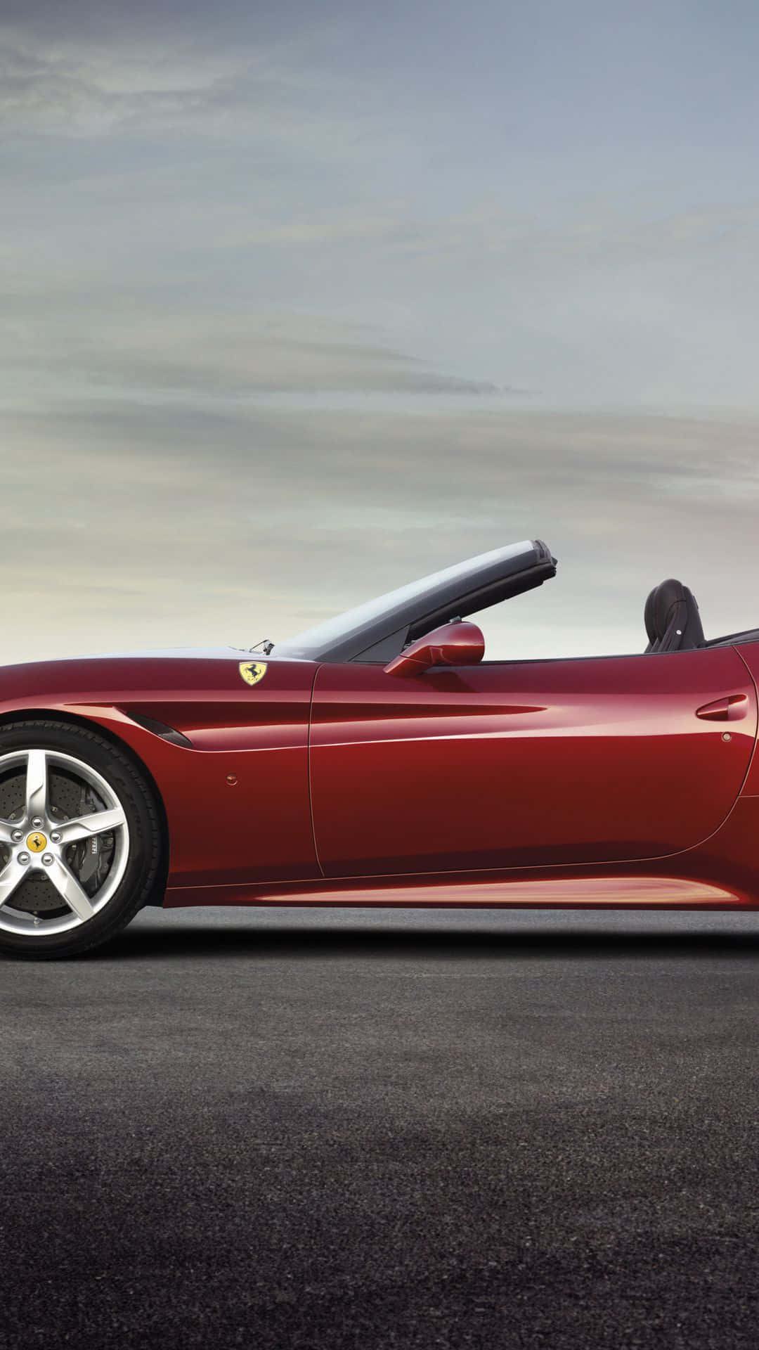Ferrari California T 桌布 壁紙 — 一架時尚的紅色法拉利敞篷車停在柏油路上，天空柔和灰色帶有雲朵。