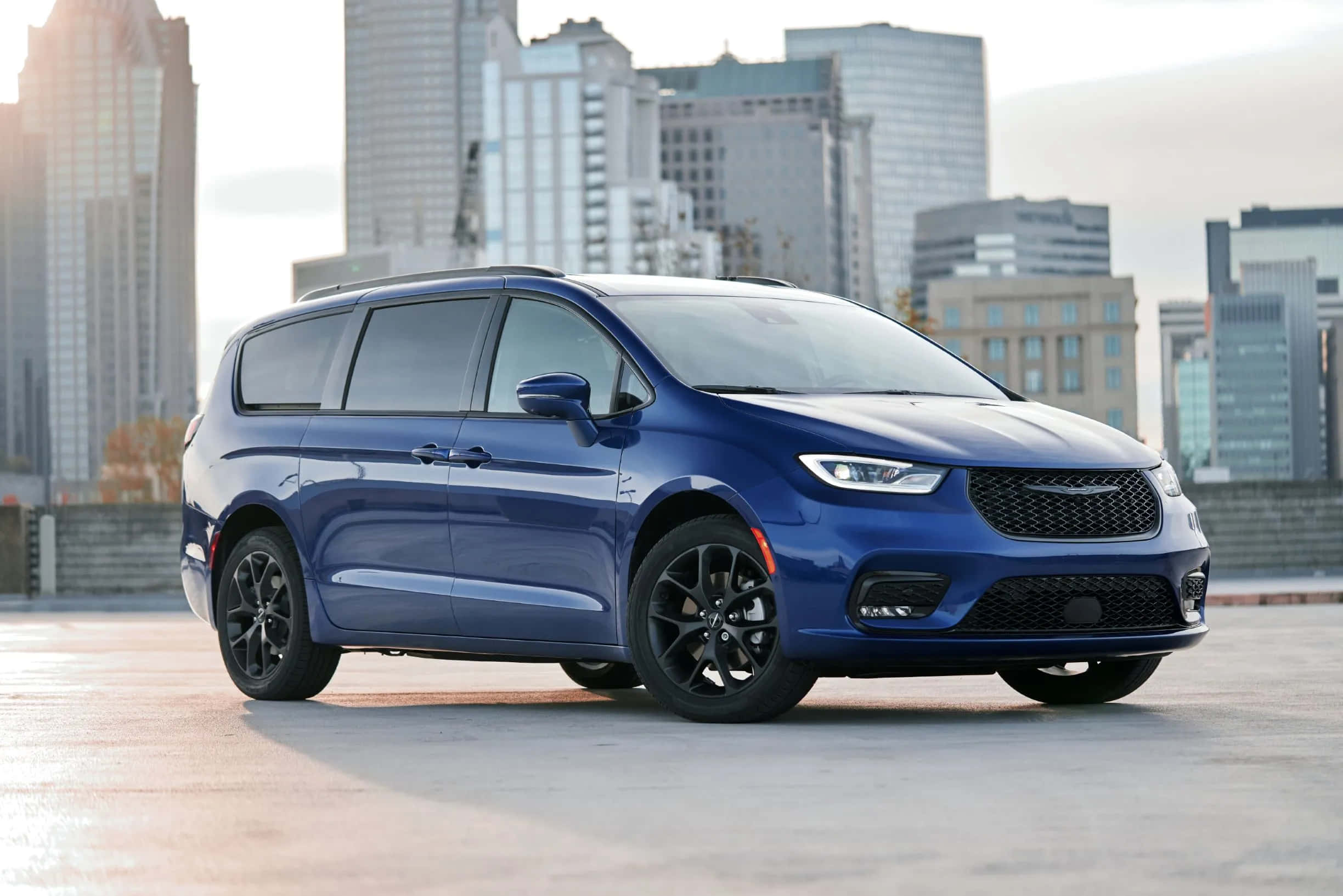 Chrysler Pacifica 桌布 壁紙 — 一架時尚的藍色小型貨車停泊在屋頂上，背景是現代城市天際線。