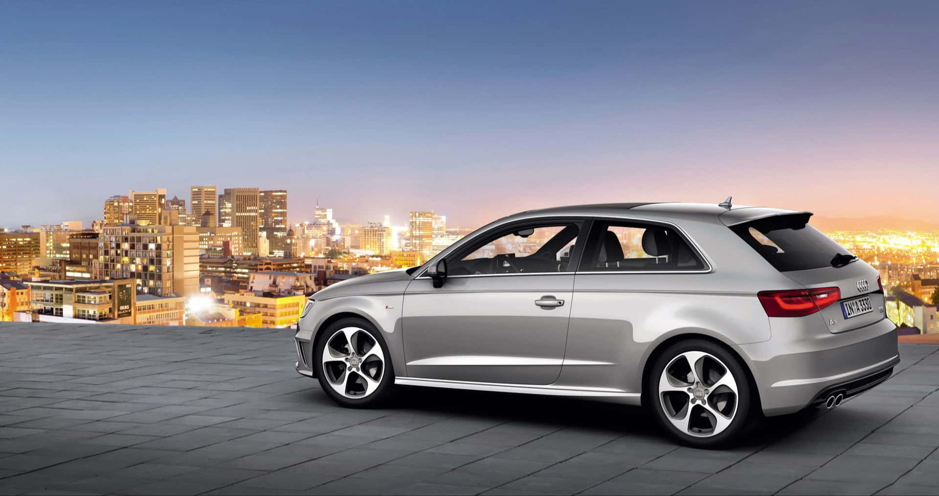 Audi A3 桌布 壁紙 — 一架時尚的銀色奧迪停在天台上，俯瞰著日落時分充滿活力的城市景觀。