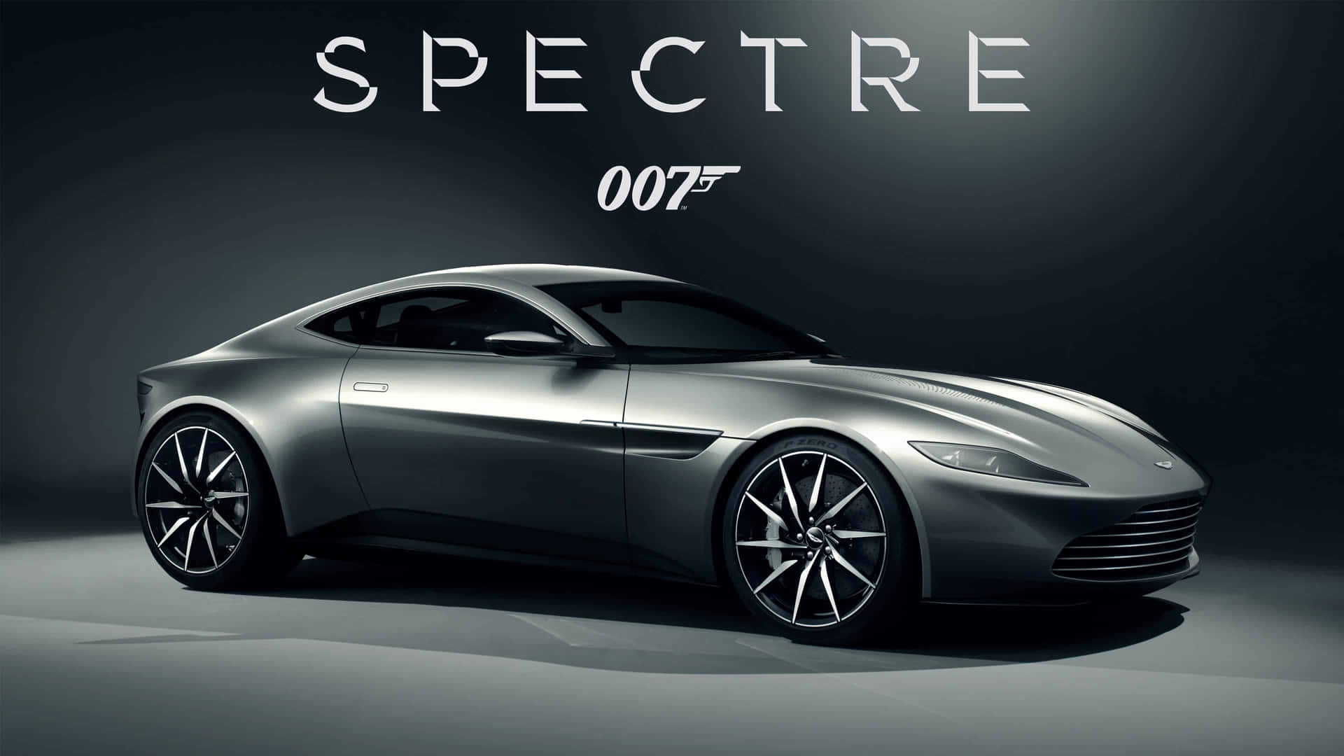  壁紙 — 一架時尚的銀色Aston Martin Spectre跑車在工作室燈光下閃耀，上方有「SPECTRE 007」文字。
