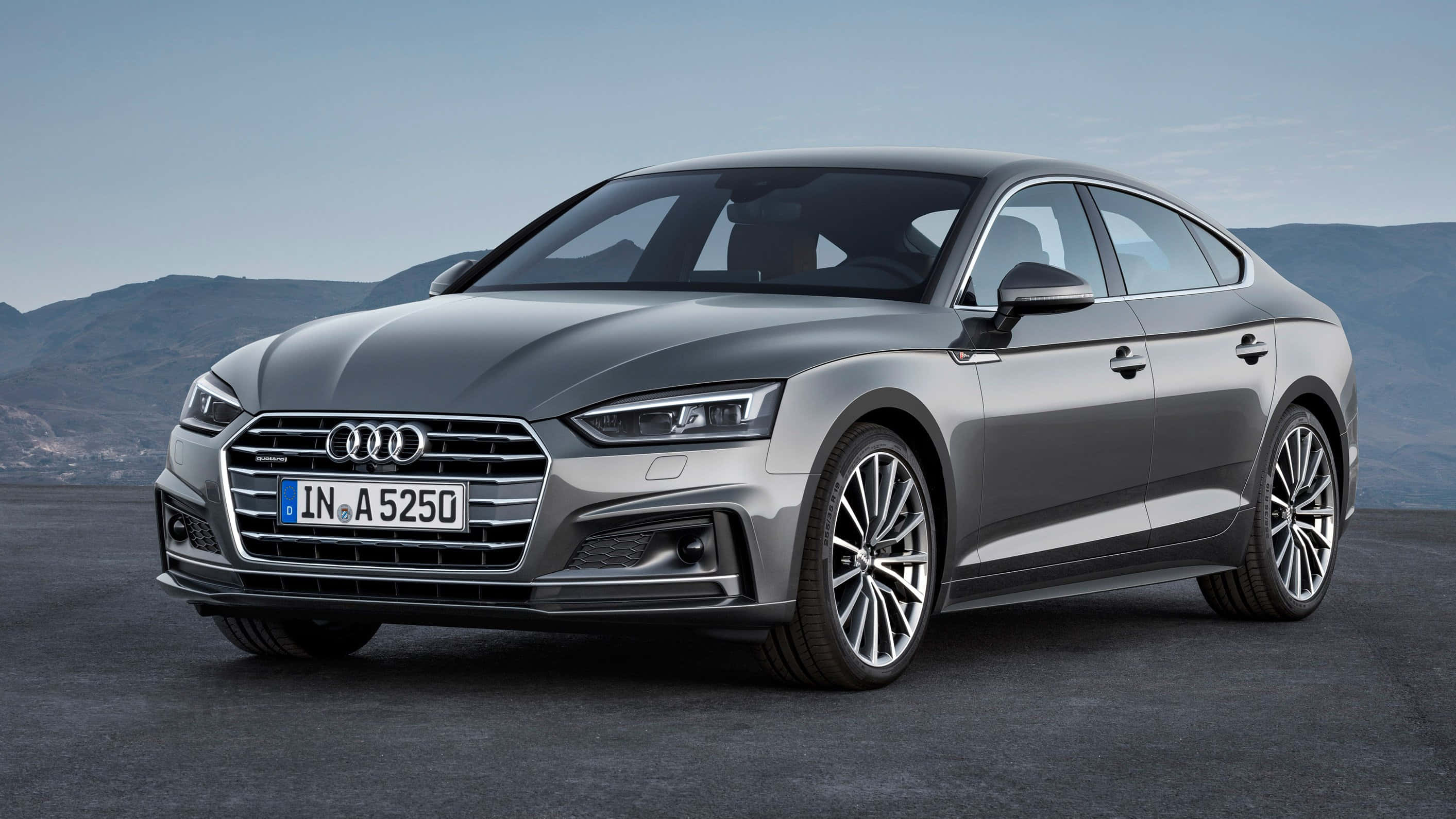 Audi A5 桌布 壁紙 — 一架時尚的銀色Audi A5 Sportback停泊在深色地面上，遠山在晴朗的藍天下。