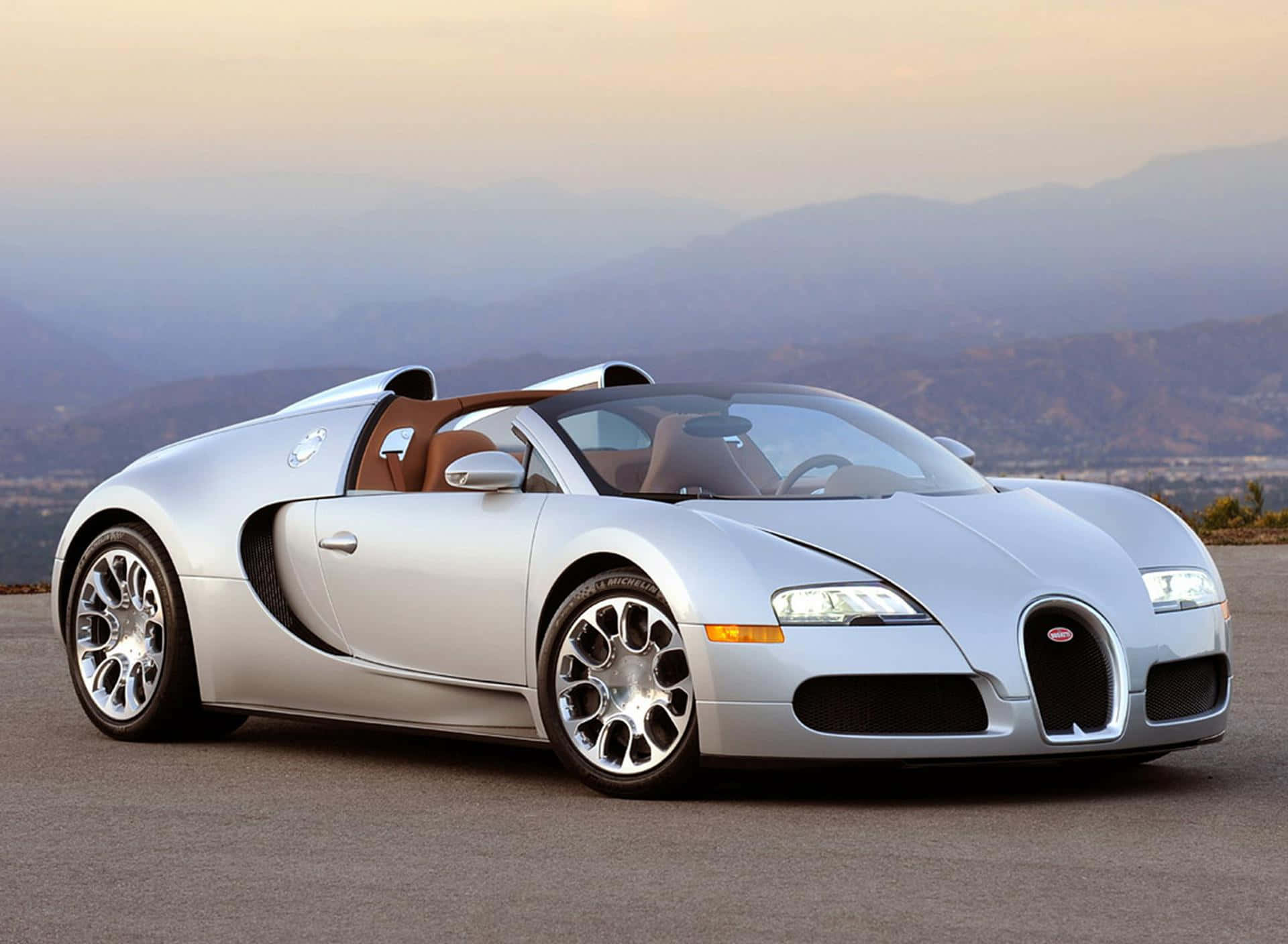Bugatti Veyron 桌布 壁紙 — 一架時尚的銀色Bugatti Veyron跑車停在鋪砌的道路上，背景是日落時分朦朧的山脈。
