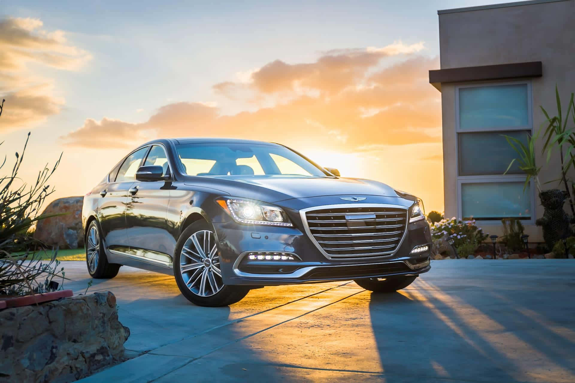 Genesis G80 桌布 壁紙 — 一架時尚的銀色轎車在金色夕陽下閃閃發光，停泊在現代房屋旁邊的混凝土車道上。