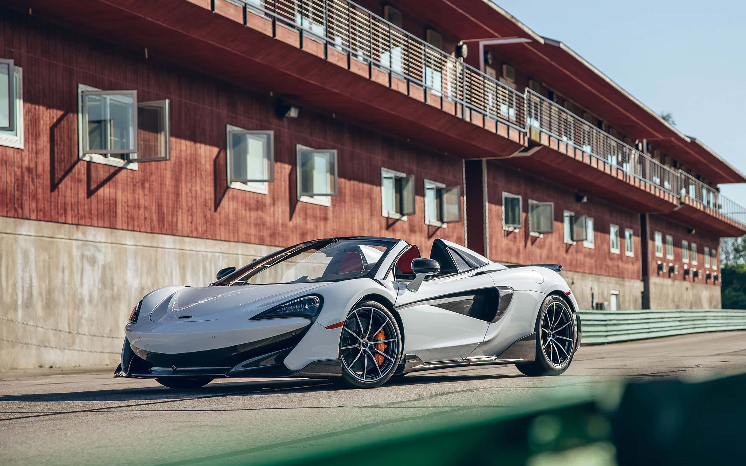Mclaren 600lt Spider 桌布 壁紙 — 一架時尚的銀色McLaren 570S Spider停泊在賽道上，旁邊是紅色木製看台，在明亮的日光下。