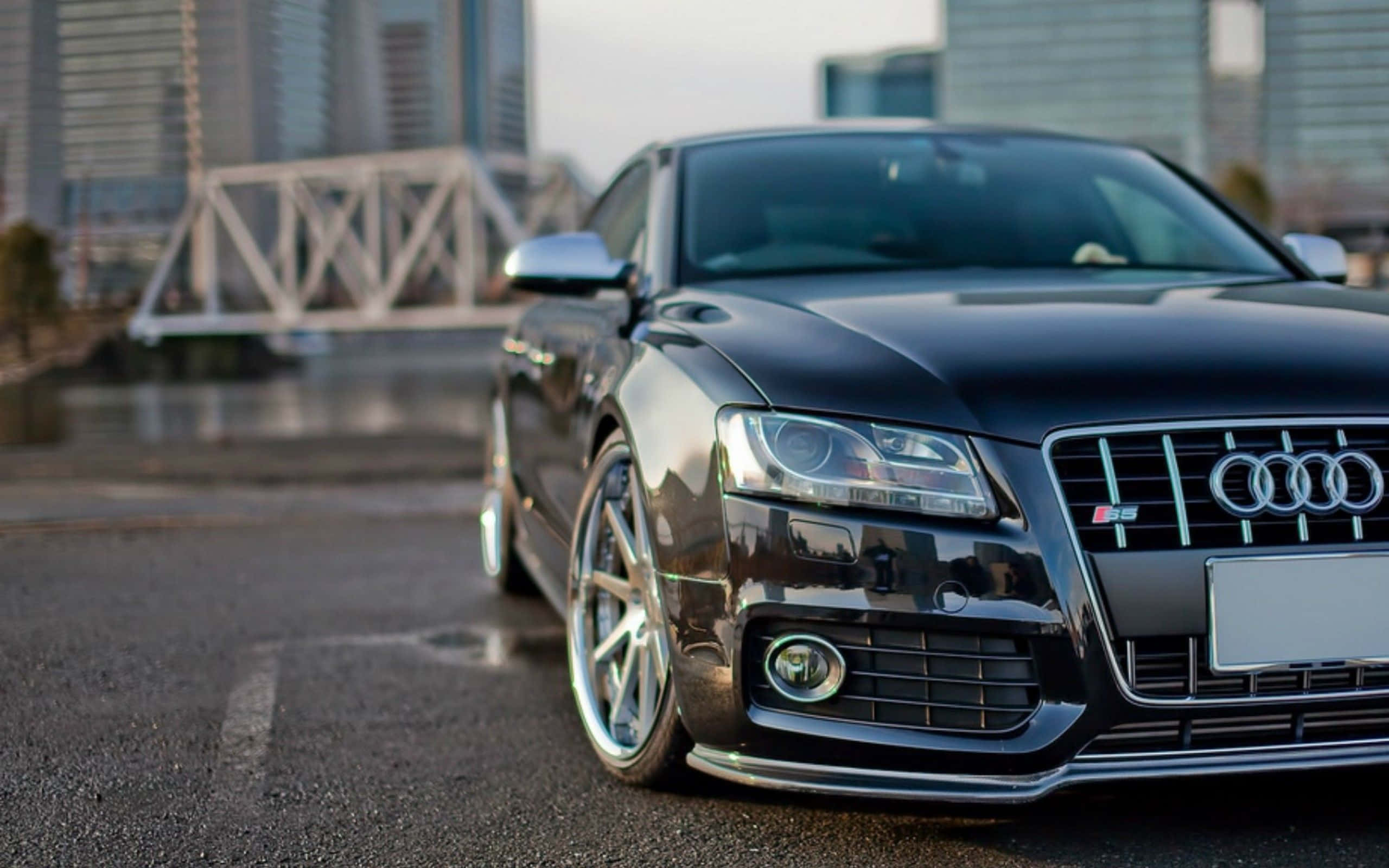 Audi S5 桌布 壁紙 — 一架時尚黑色Audi S5跑車停泊在濕潤的城市街道上，背景有現代橋樑和摩天大樓。