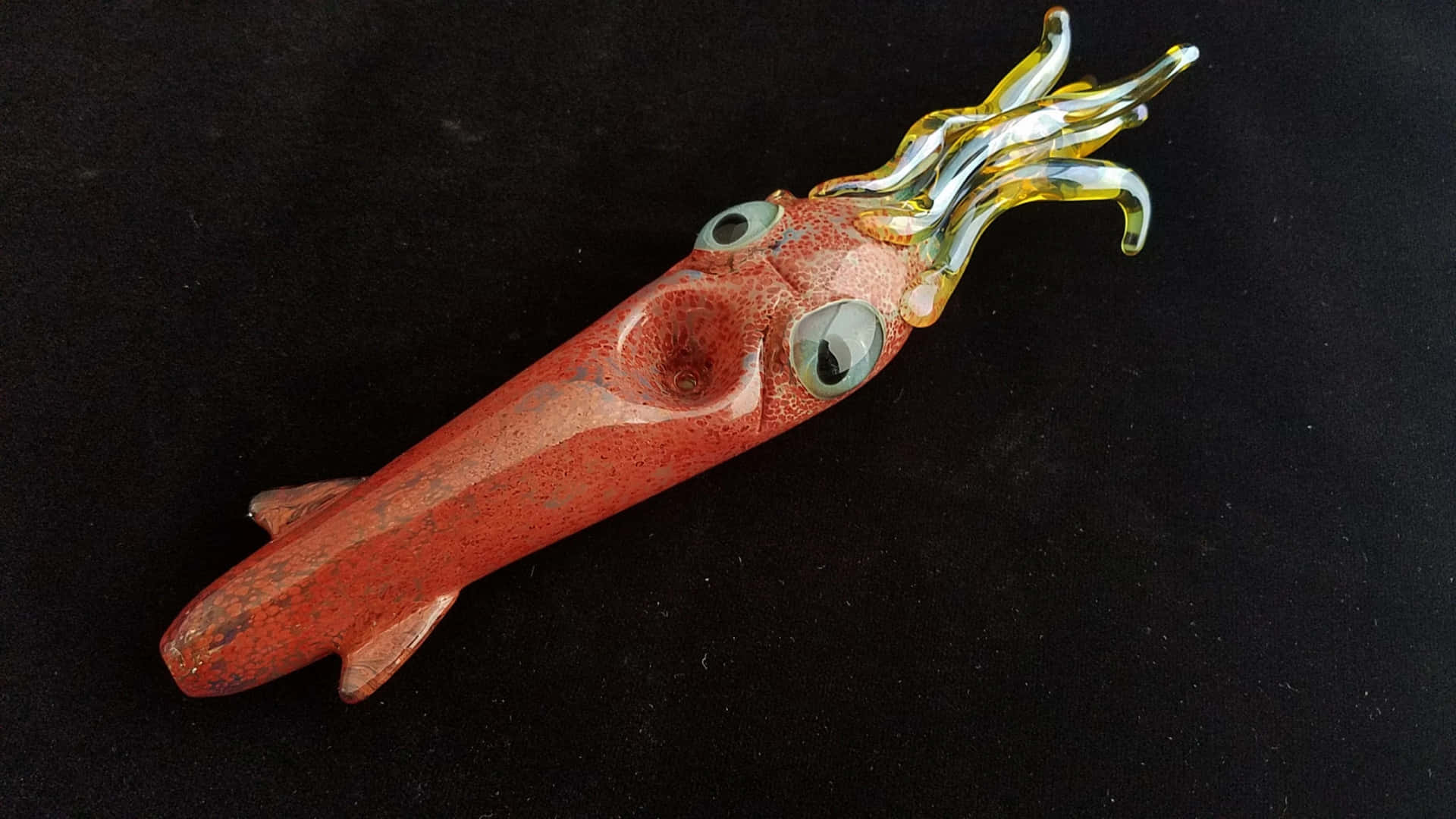  壁紙 — 一件手工製作的玻璃魷魚雕塑，紅色身體和黃色觸手，放置在黑色背景上。