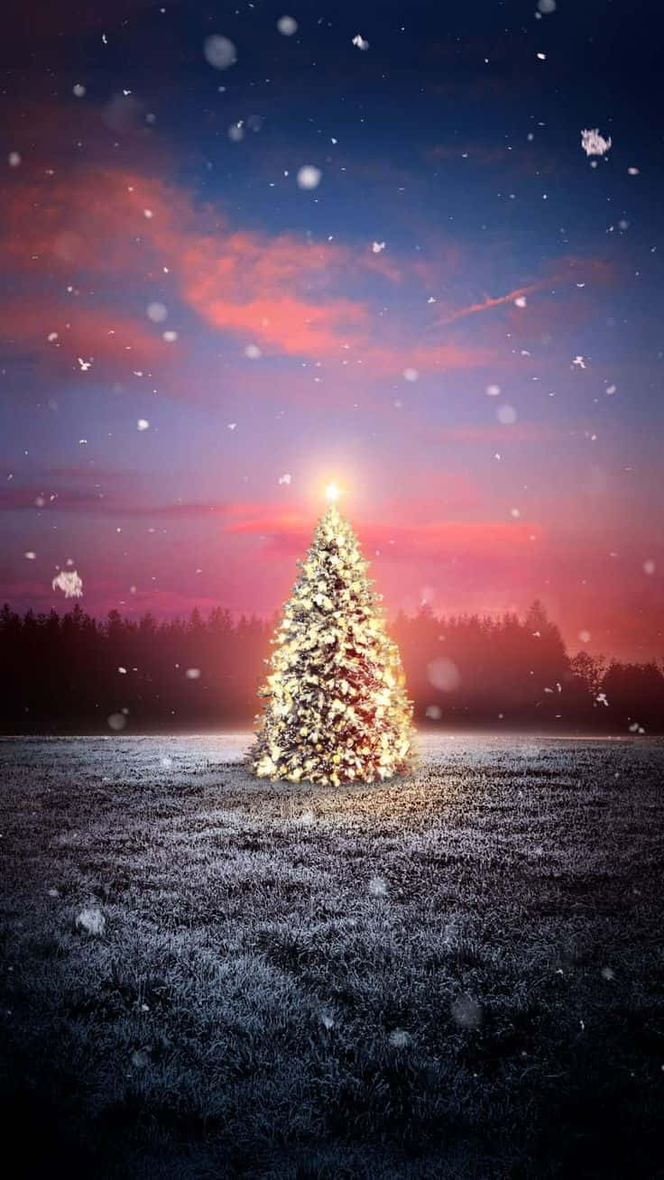  壁紙 — 一棵發光的聖誕樹獨自矗立在雪地上，背景是充滿活力的暮色天空，雪花飄落。