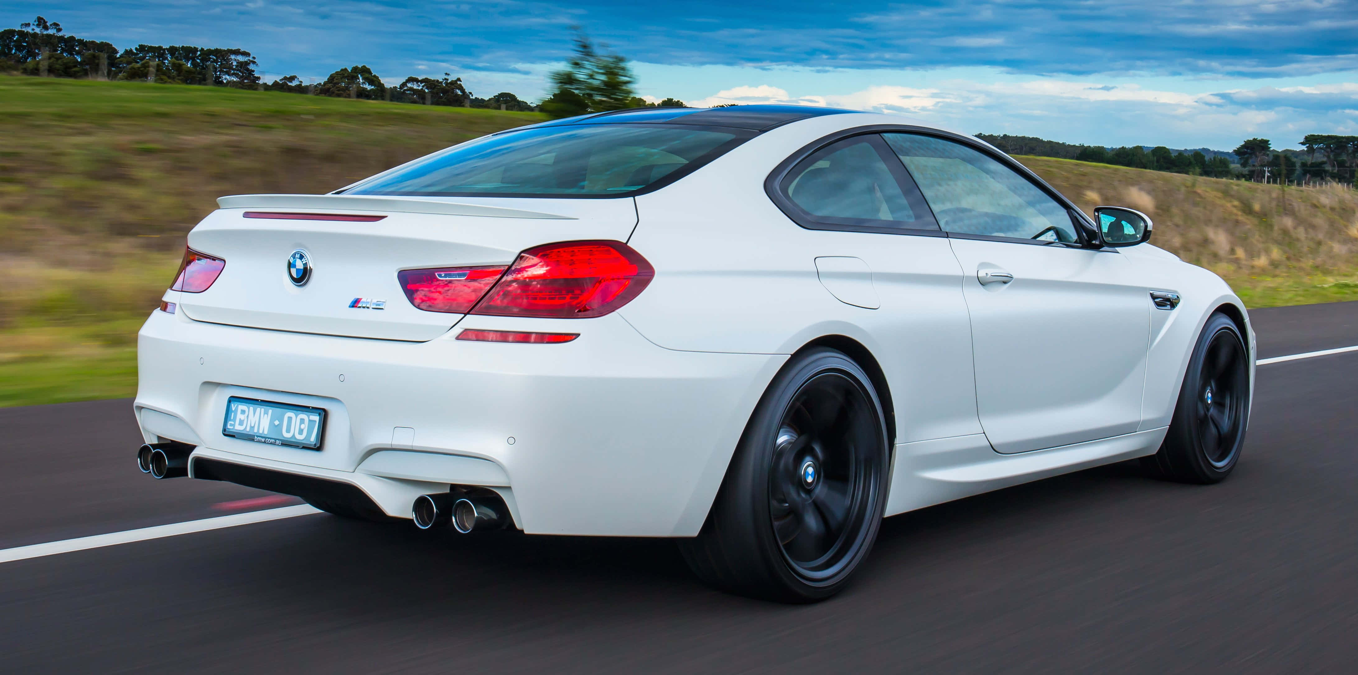 Bmw M6 桌布 壁紙 — 一輛白色BMW M6雙門跑車在鄉村道路上疾馳，背景是模糊的綠色田野和藍天。