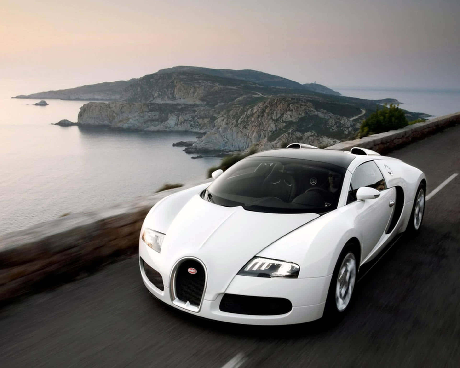 Bugatti Veyron 桌布 壁紙 — 一輛白色Bugatti Veyron在日落時分沿著懸崖和海洋背景的海岸道路飛馳。