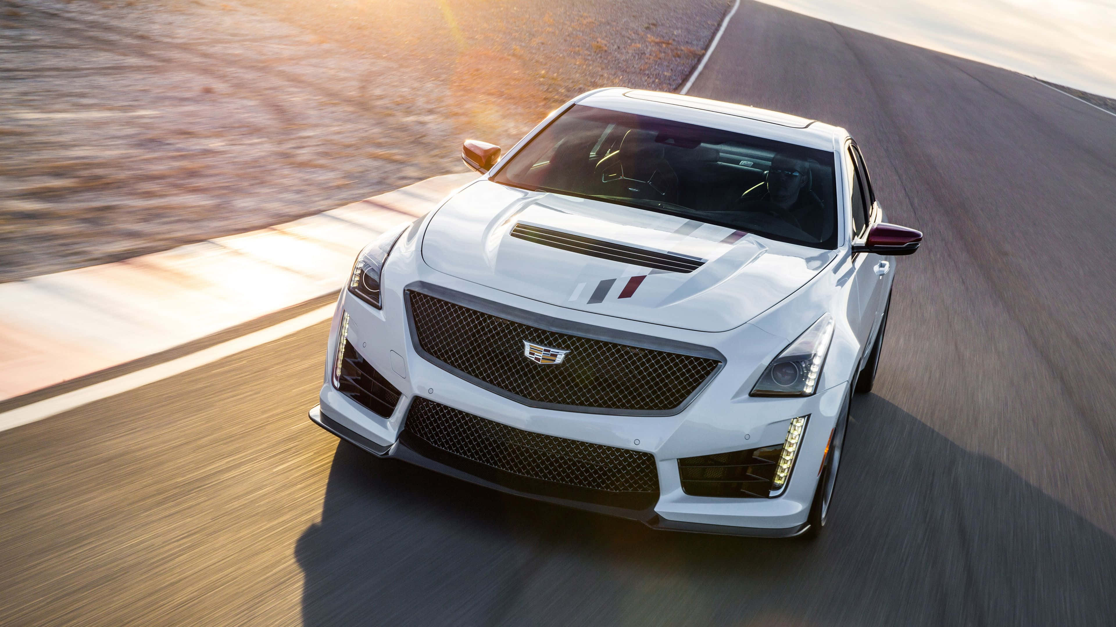 Cadillac Cts 桌布 壁紙 — 一輛白色Cadillac ATS-V在日落時分沿著蜿蜒的道路疾馳，動態模糊強調了其動力和流線型設計。