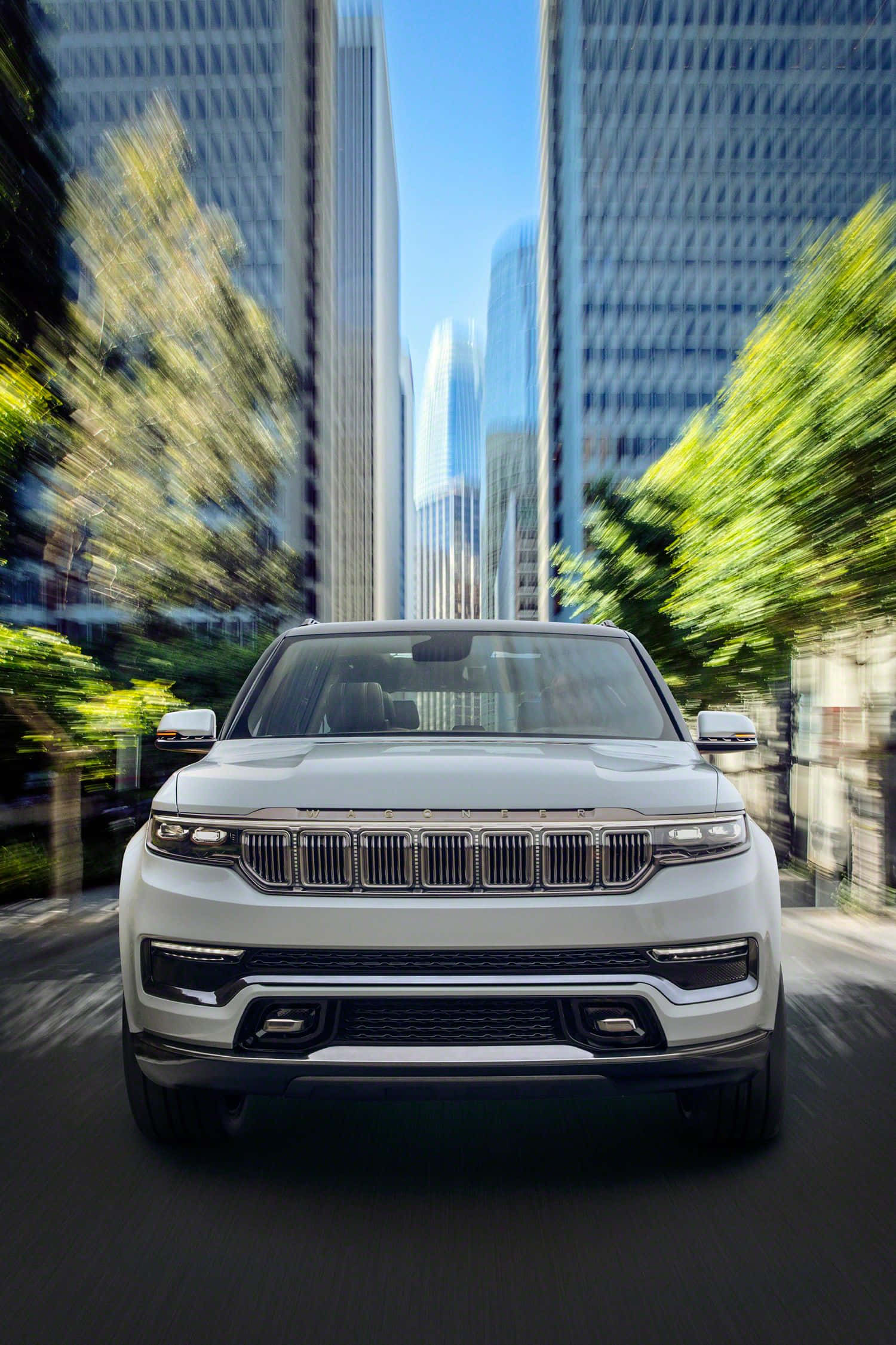 Jeep Wagoneer 桌布 壁紙 — 一輛白色豪華SUV在綠樹成蔭的城市街道上飛馳，摩天大樓和綠植呈現動態模糊效果。