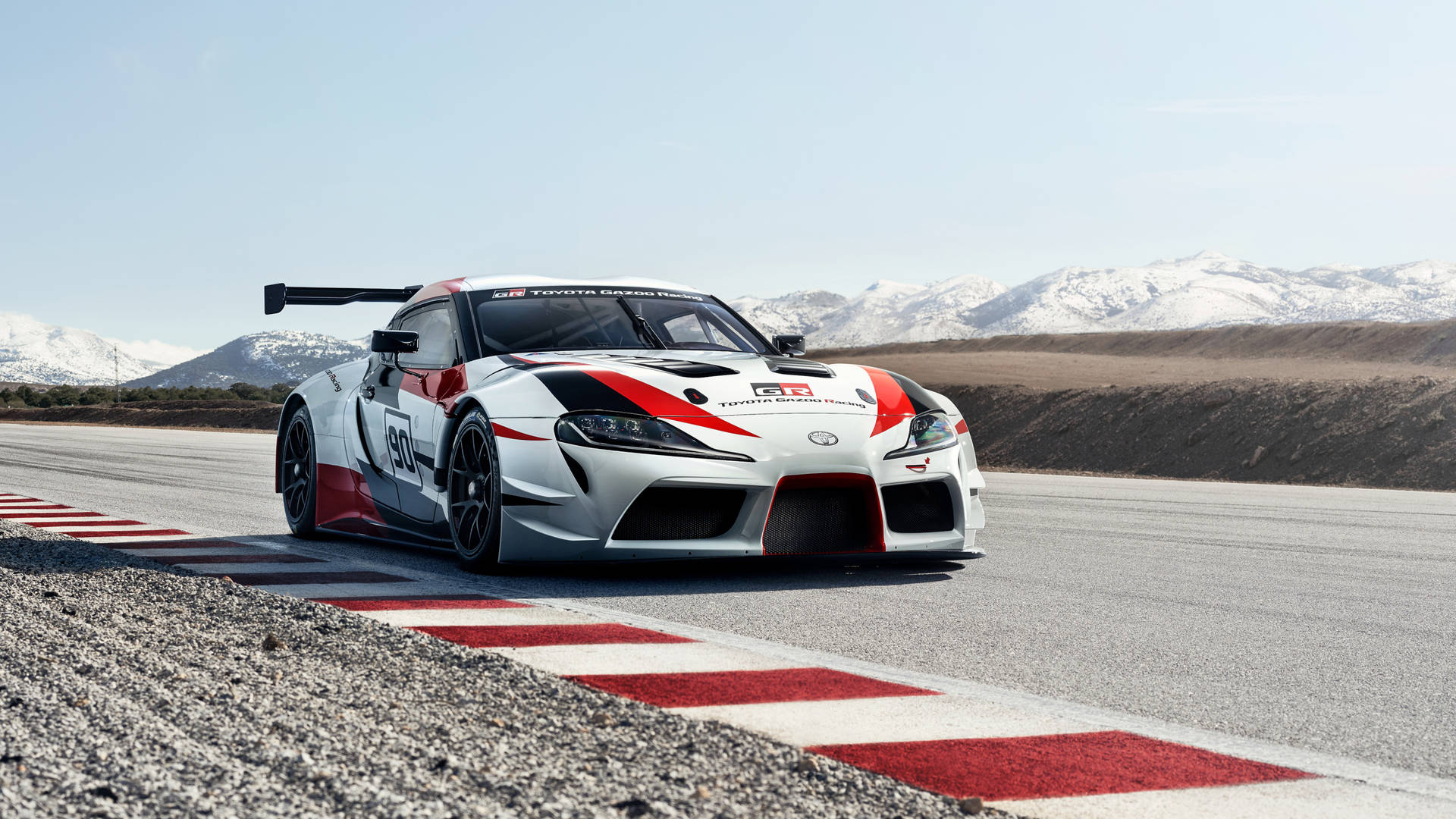 白色、紅色和黑色的賽車在賽道上，背景有白雪覆蓋的山脈。 — Toyota Supra 壁紙