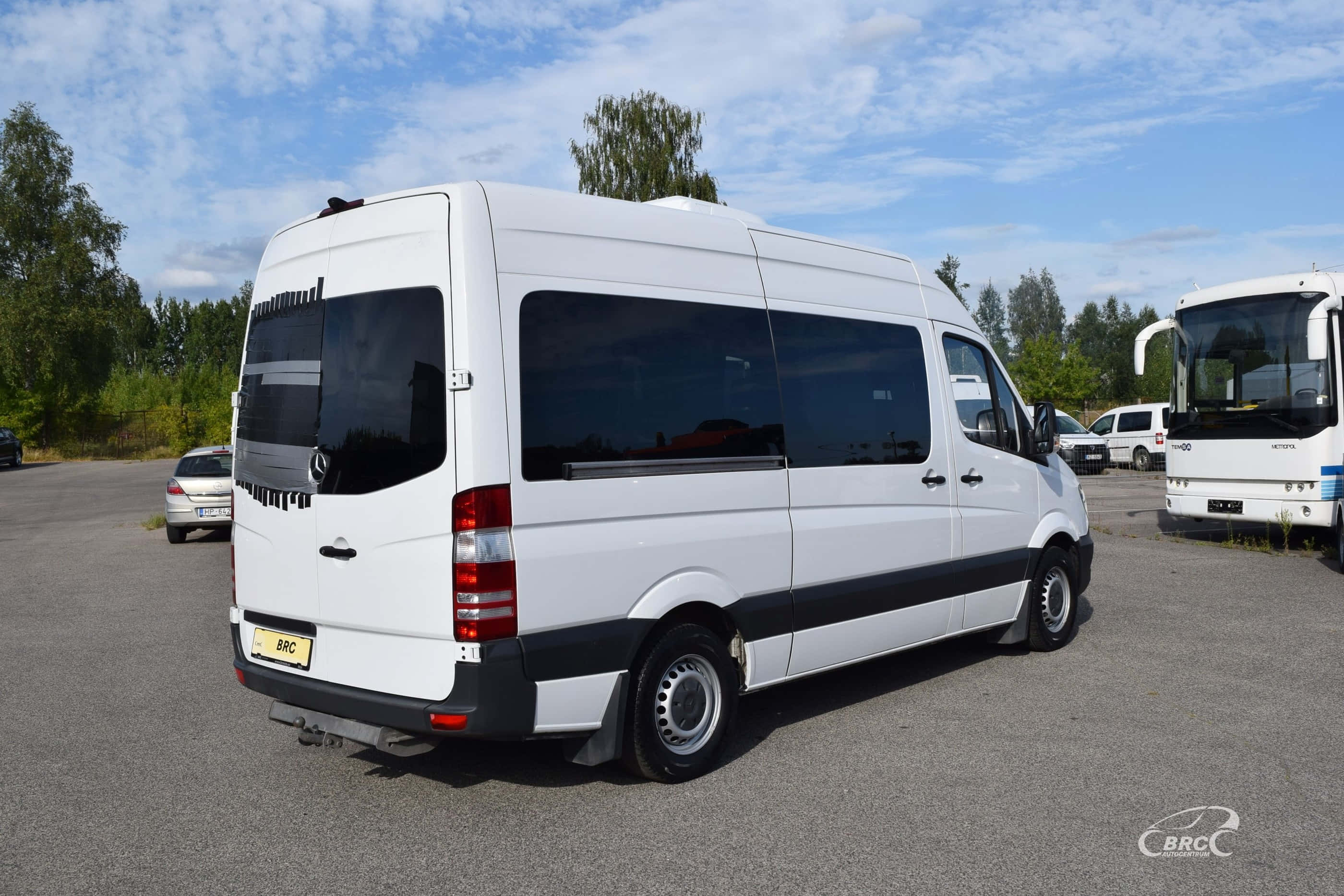 Mercedes Benz Sprinter 桌布 壁紙 — 一輛白色 Mercedes-Benz Sprinter 客貨車停放在停車場，天空局部多雲，附近有樹木及其他車輛。