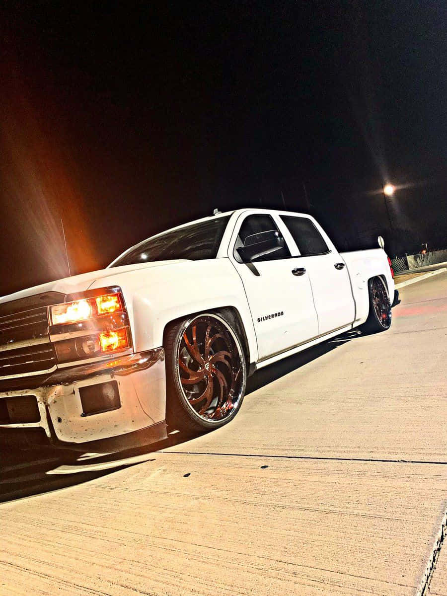  壁紙 — 一輛白色升高的Chevrolet Silverado pickup truck，配備定制青銅輪圈，夜晚停放在混凝土場地，在人造燈光下。