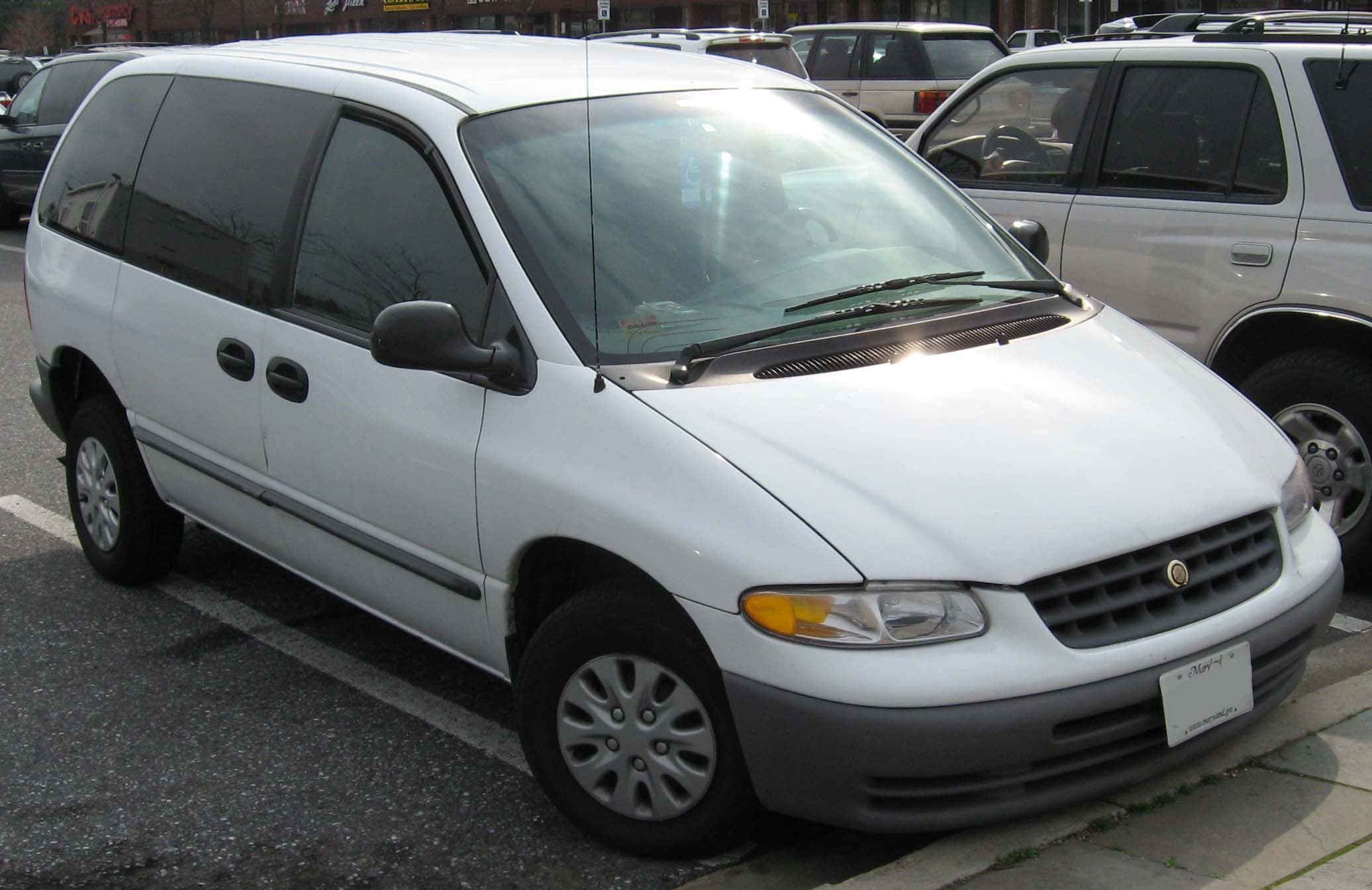 Chrysler Voyager 桌布 壁紙 — 一輛白色小型貨車停放在停車場，與其他車輛一起在明亮的日光下。